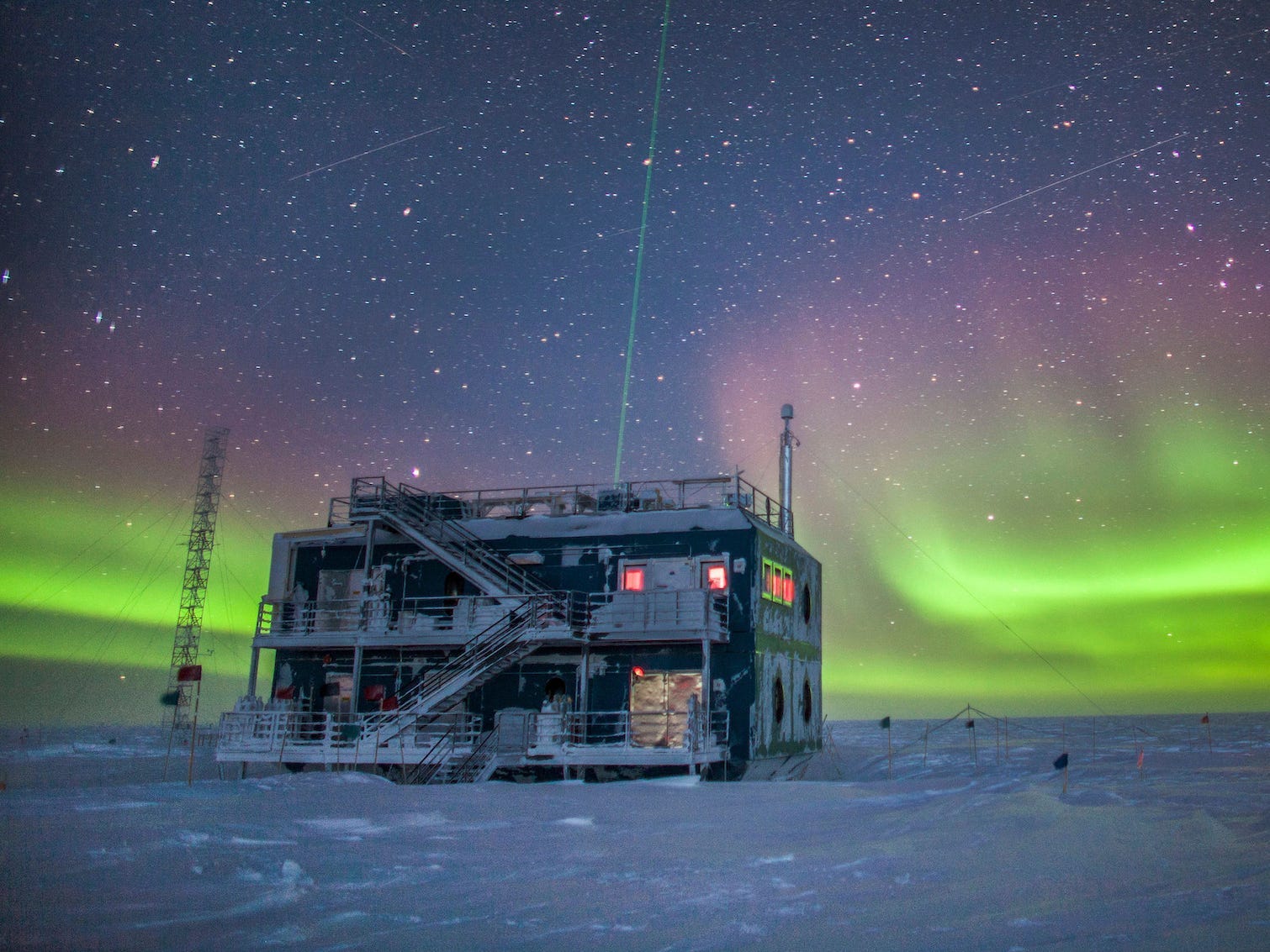 The Atmospheric Research Observatory,  two-storied industrial building, is pictured here at night in 2018 in front of green auroras lighting up the sky in the background.