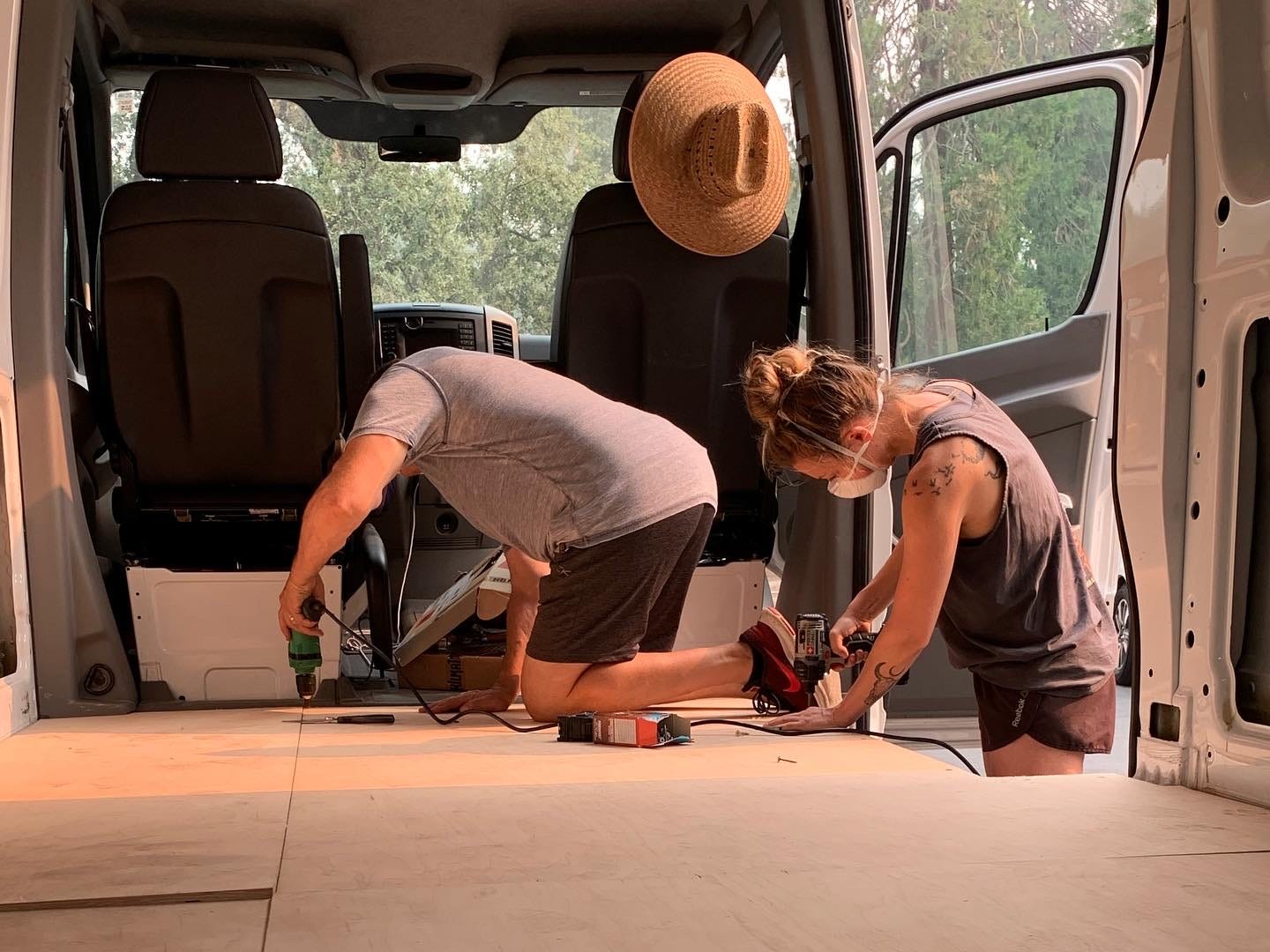 A man and a woman use tools to fit a wooden floor into a white van.