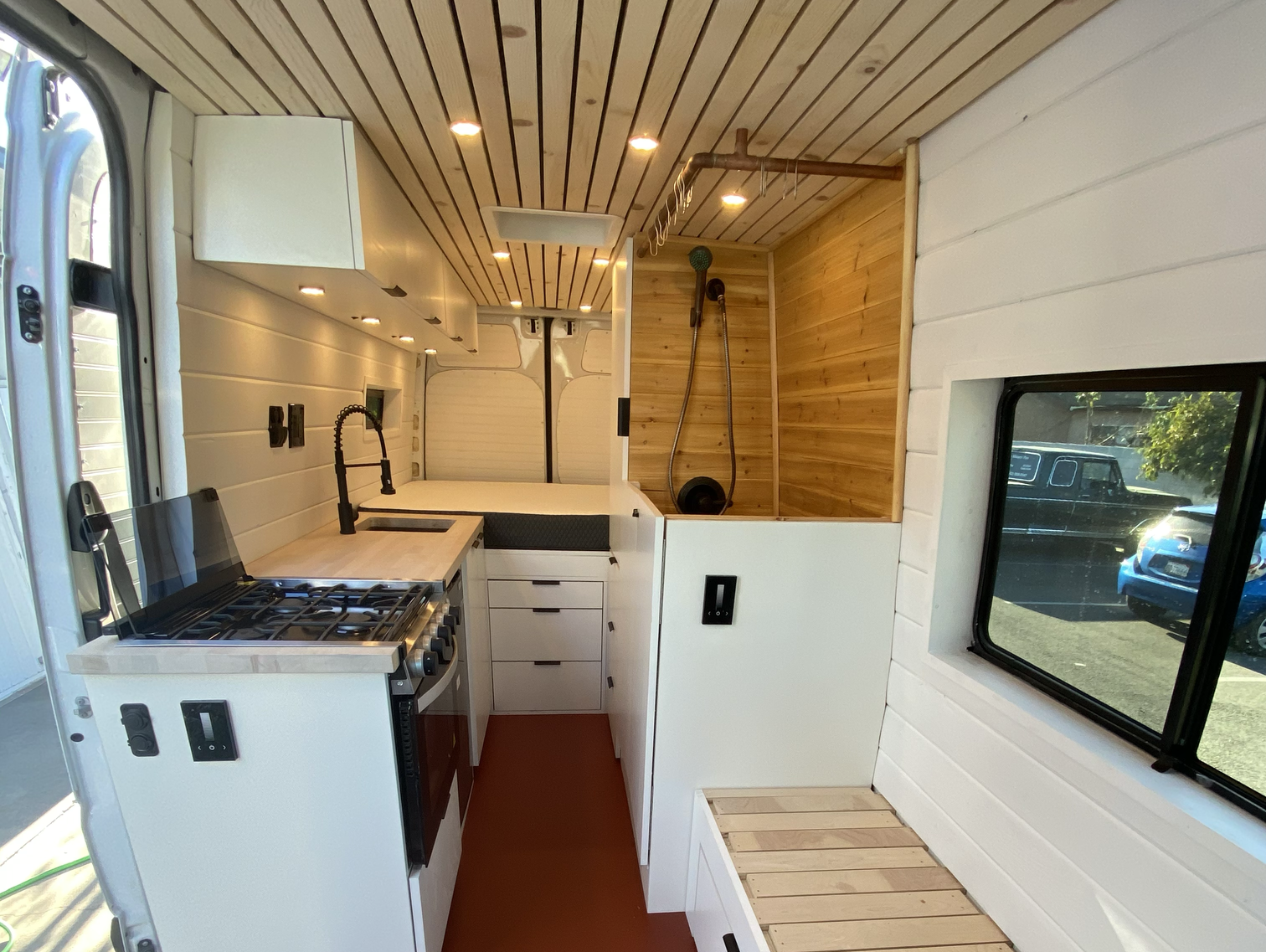 The interior of a white van with a kitchen, bench, bed and shower.