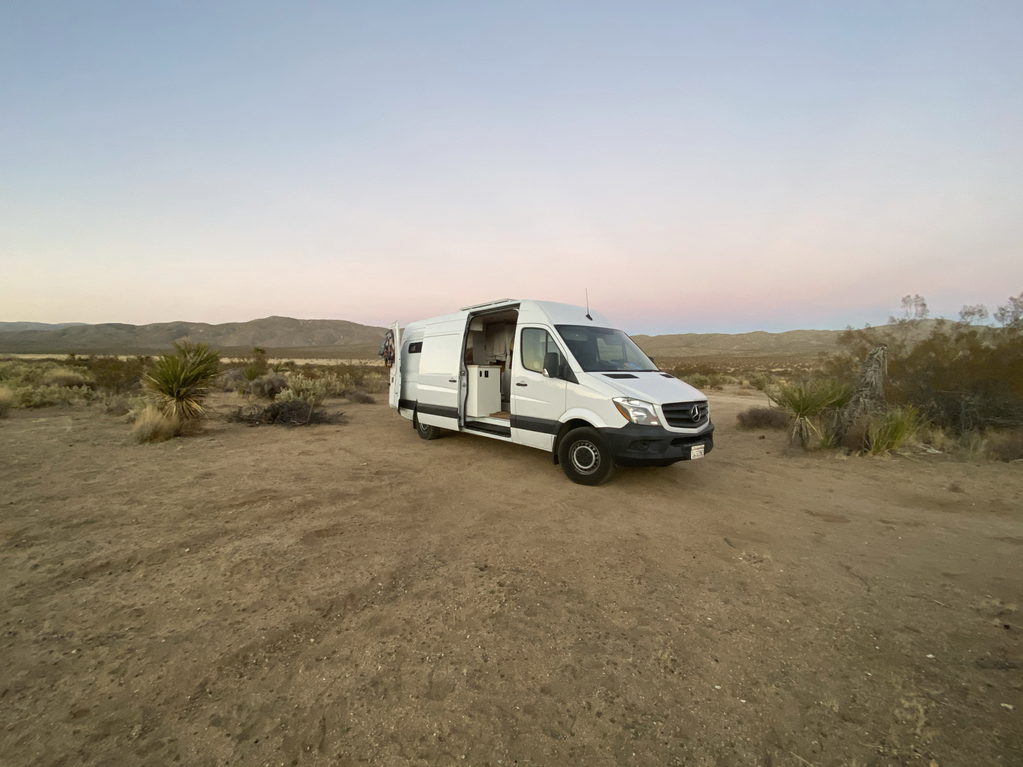 A white van sits in the middle of a desert in early evening.