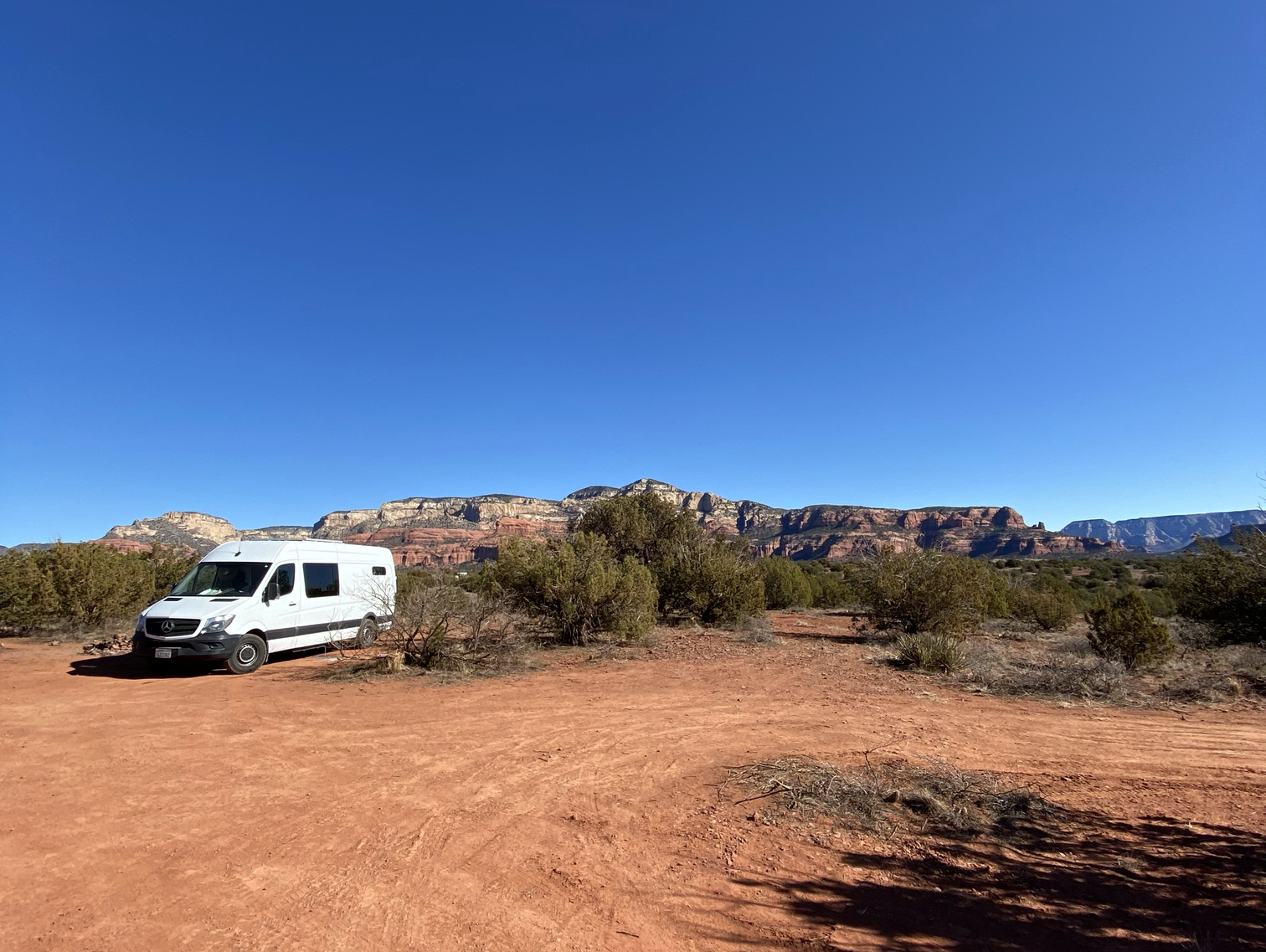 A white van sits in a desert with orange colored sand and a bright blue sky.