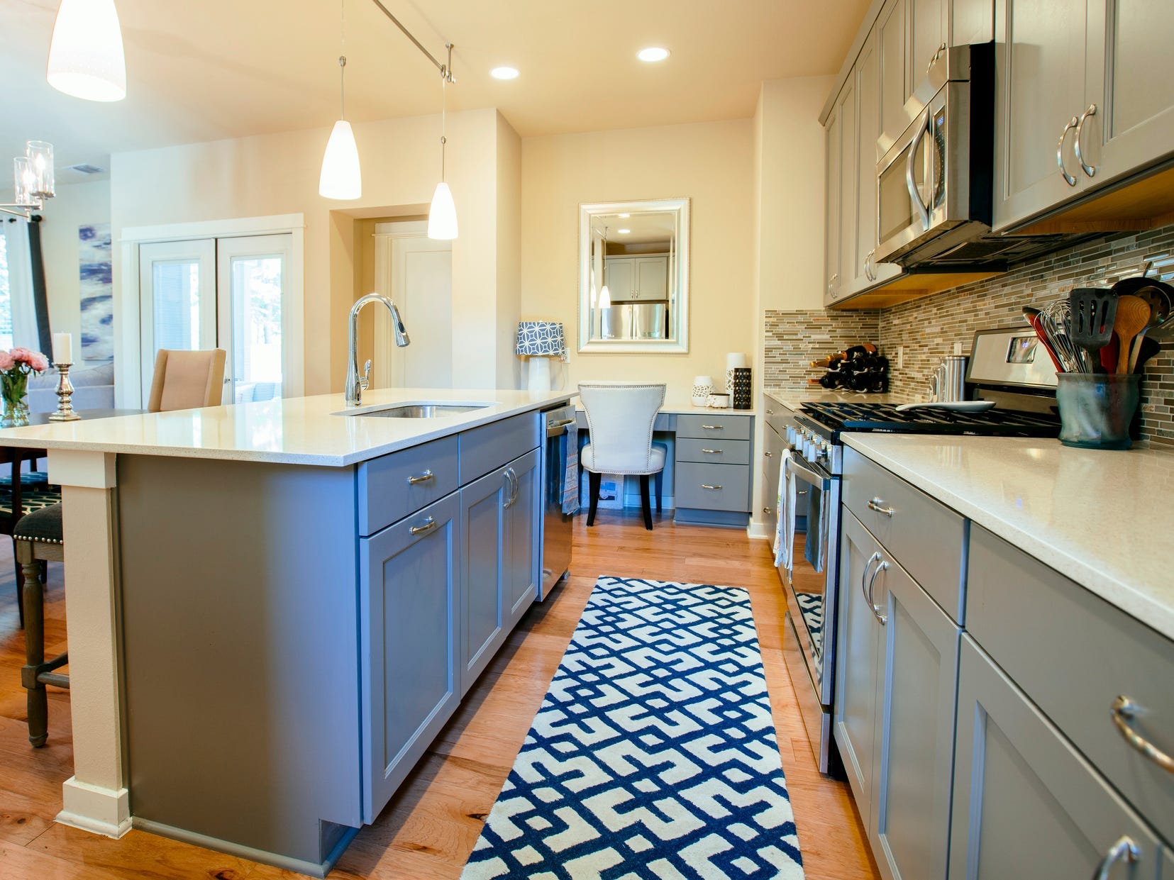 The interior of a kitchen with gray cabinets, white countertops, a gray island, and a blue rug in between them