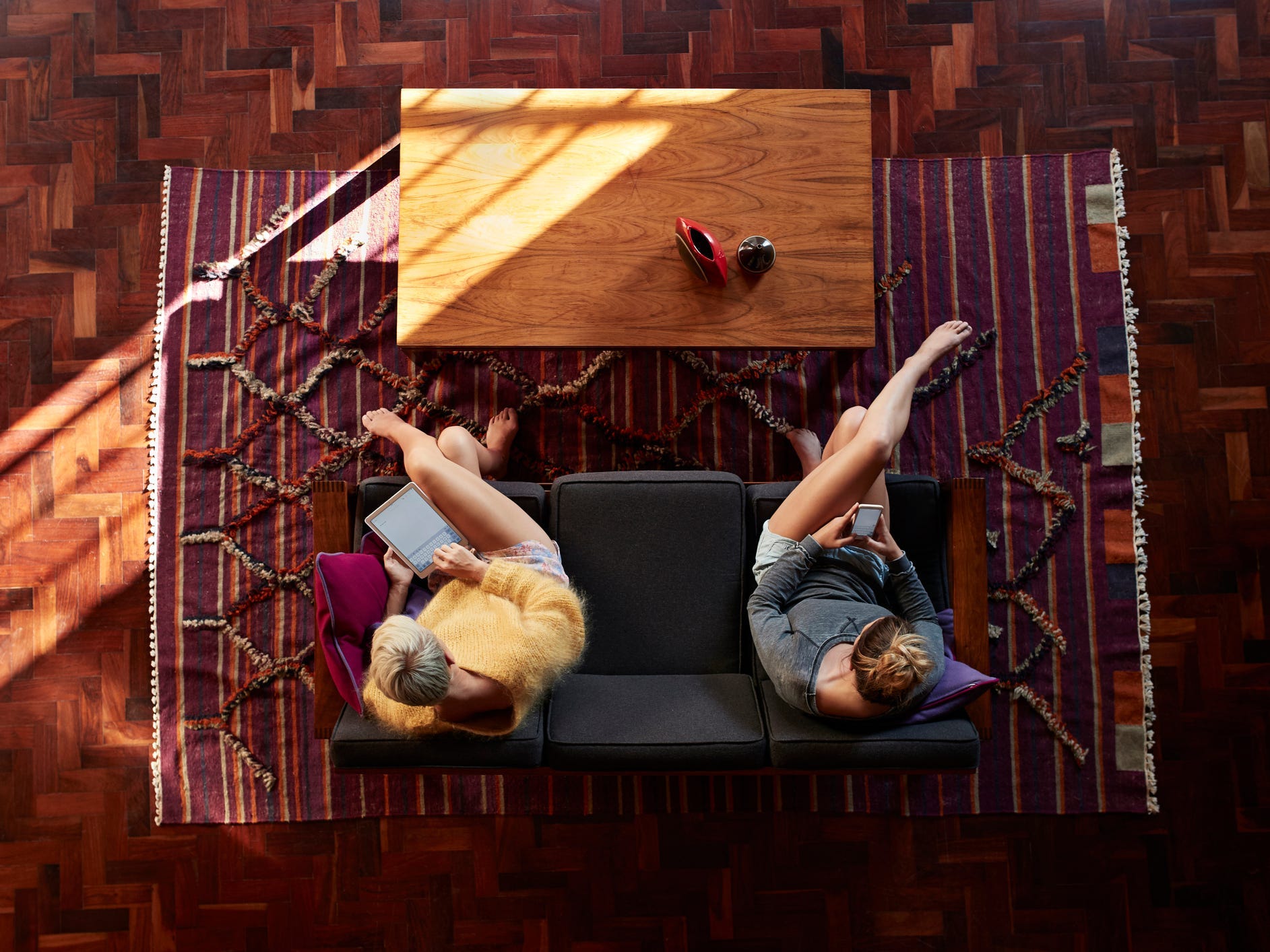 A view from above of two people sitting on a couch on top of a colorful area rug