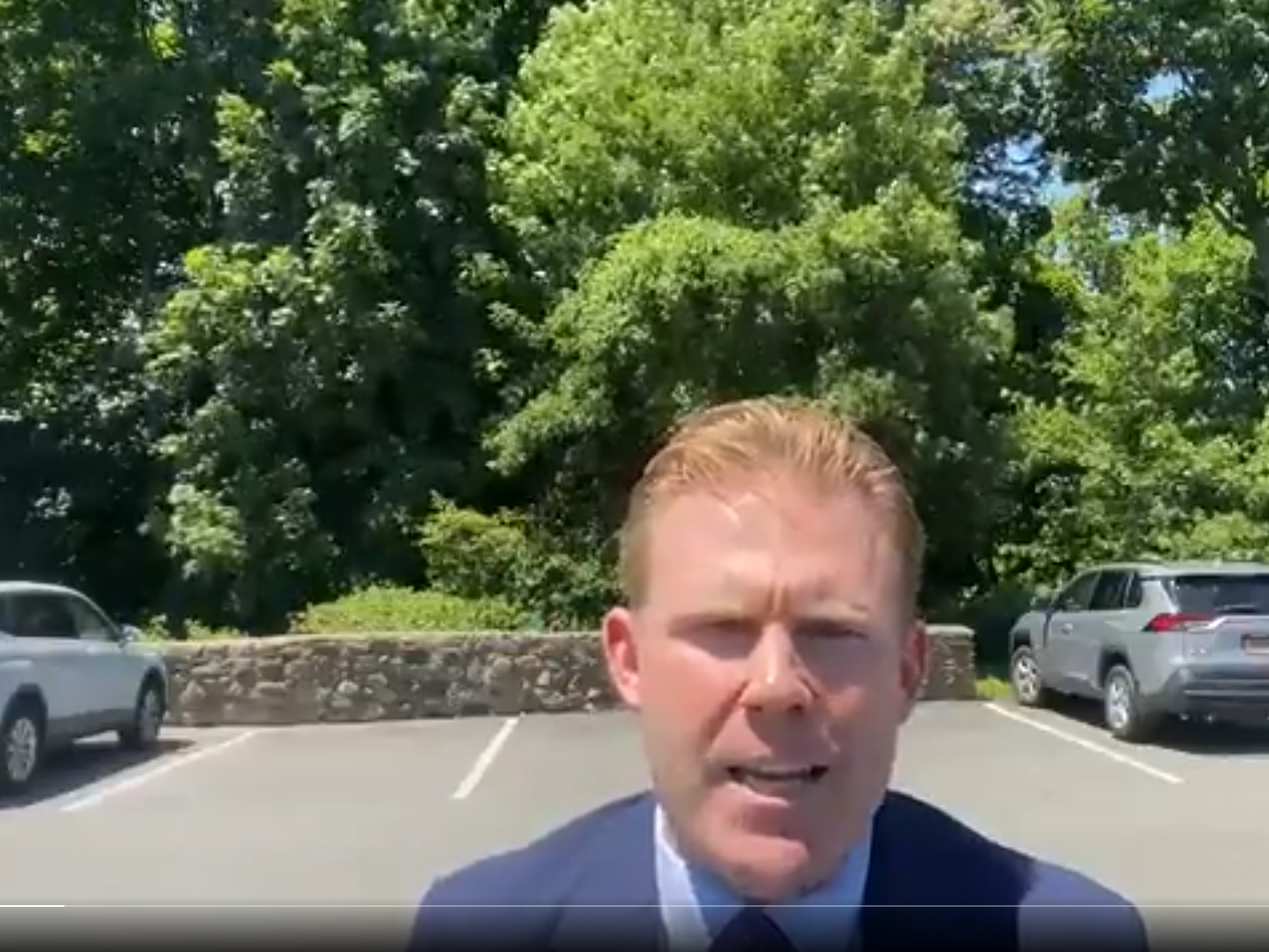 Screenshot of a video of Andrew Giuliani speaking to the camera from a parking lot framed by two SUVs and greenery in the background.