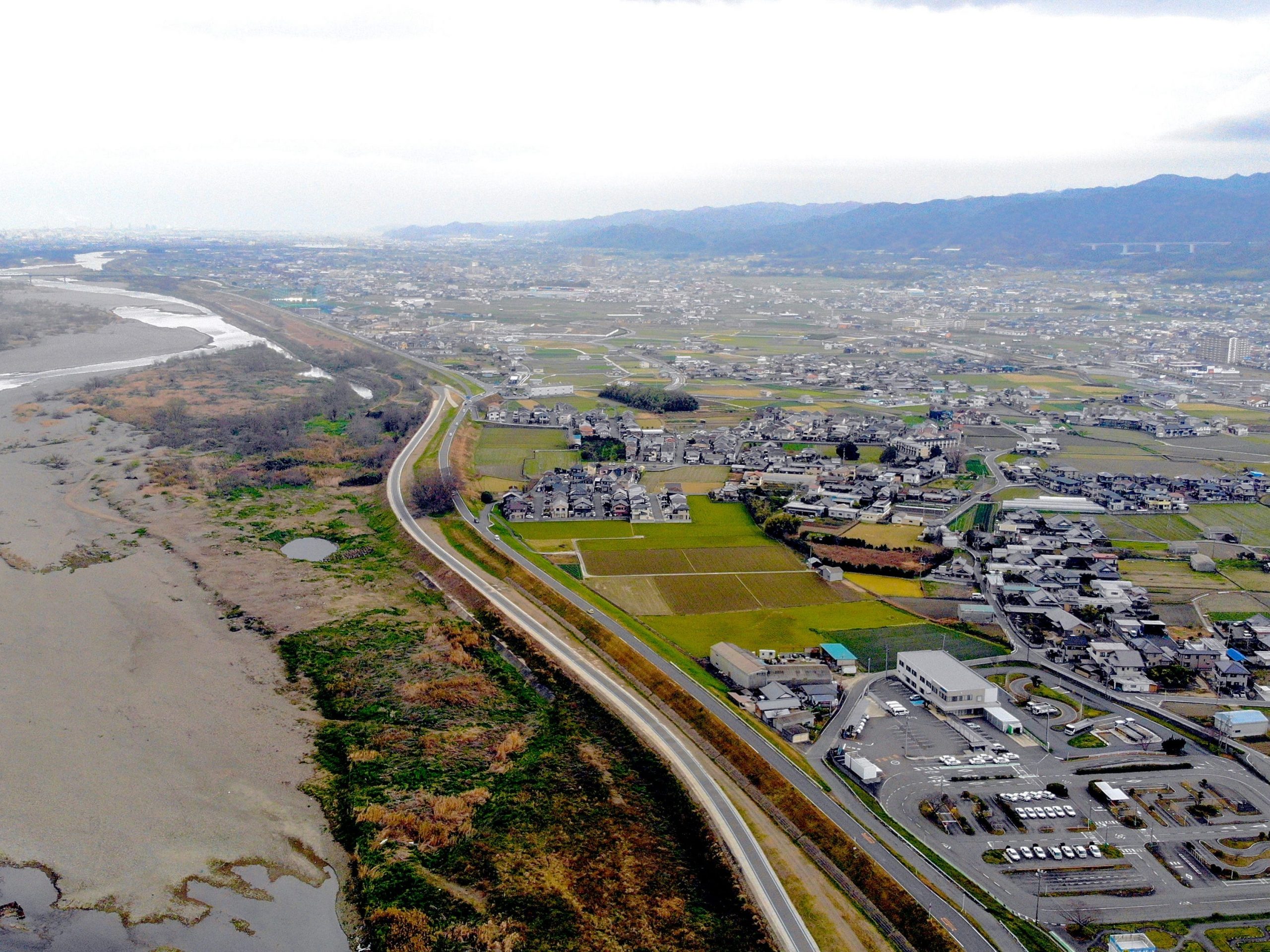A drone photograph of Iwade-shi shows sprawling fields and a wide river next to a house.