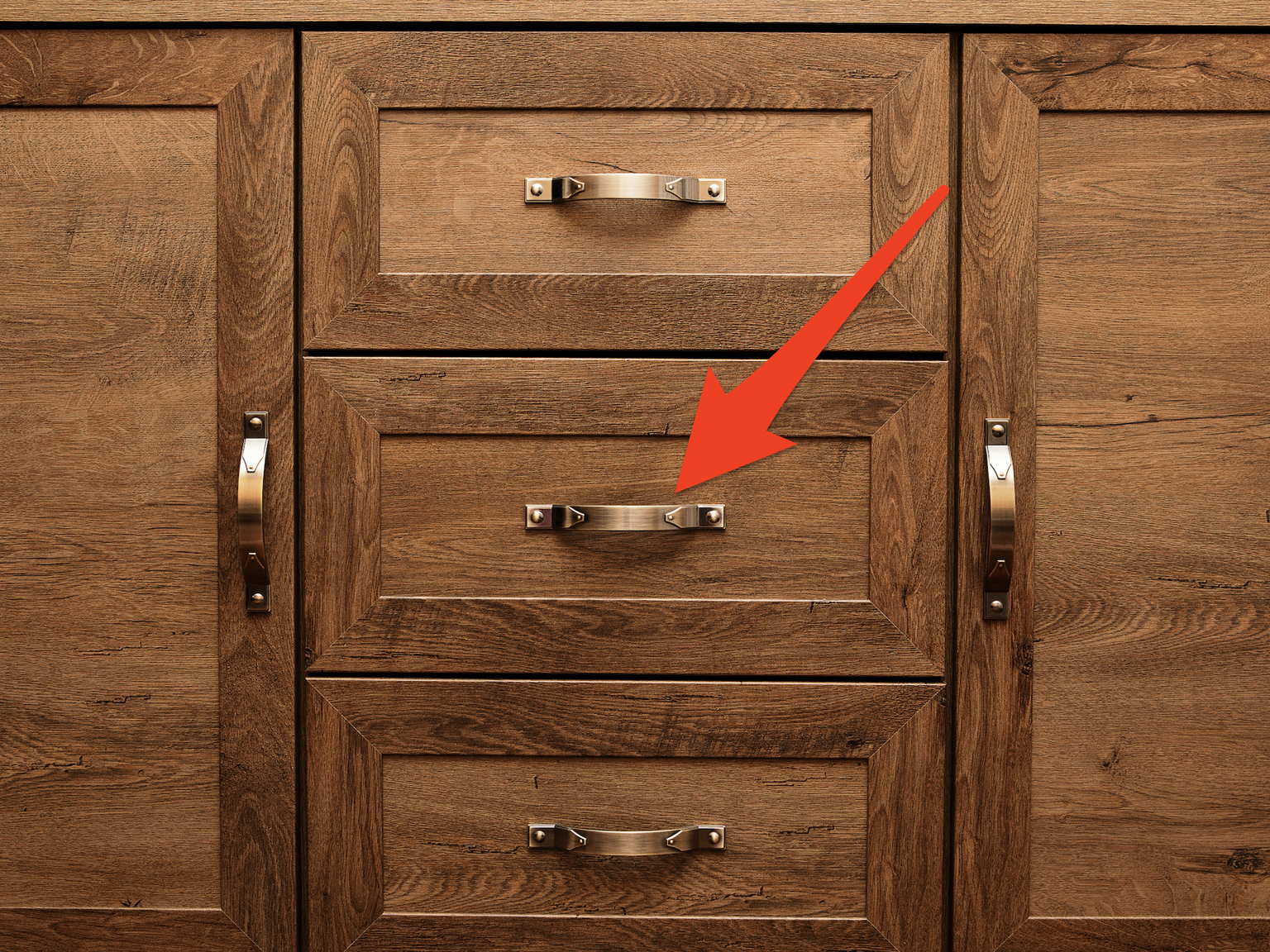 arrow pointing to gold hardware on piece of wooden furniture