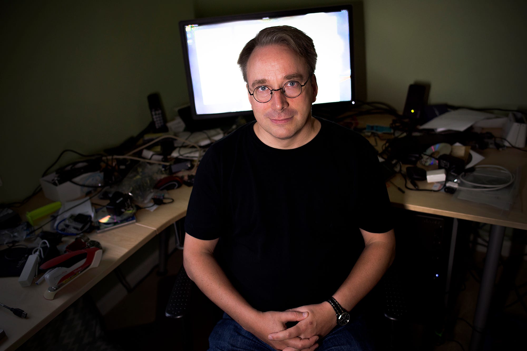 Linus Torvalds wearing a black T shirt sitting in his office in front of a computer screen