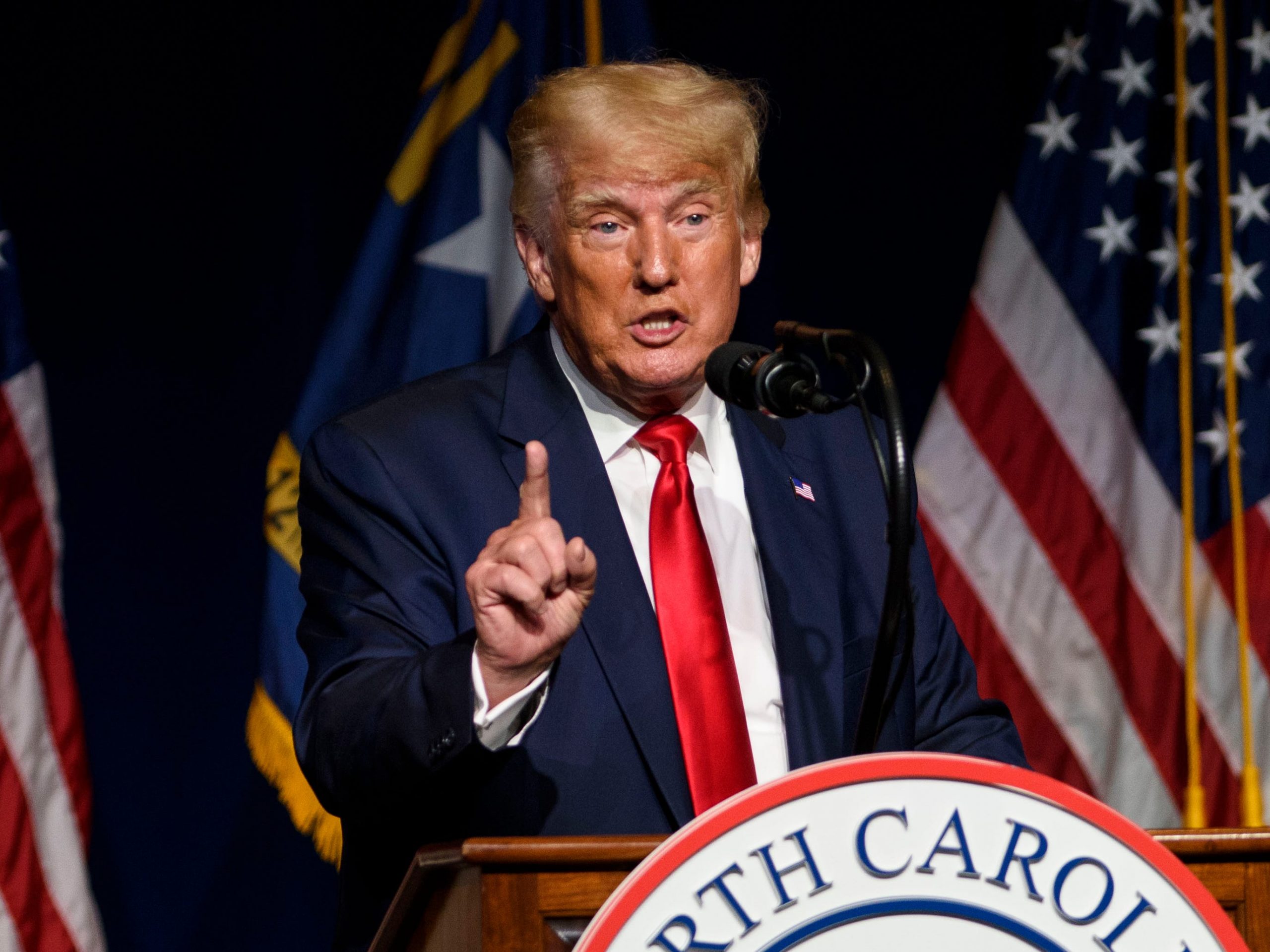 Donald Trump speaks at a podium in front of American flags.