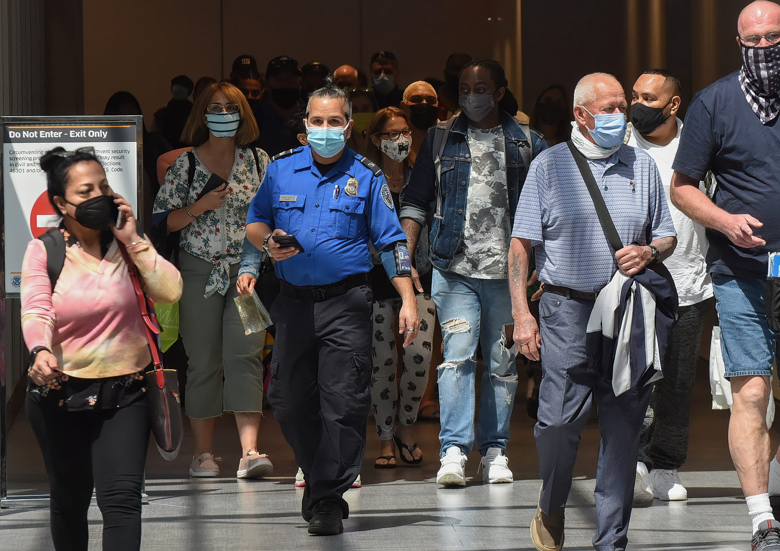 A Transportation Security Administration officer wearing a blue shirt walks through an airport with lots of passengers around him.