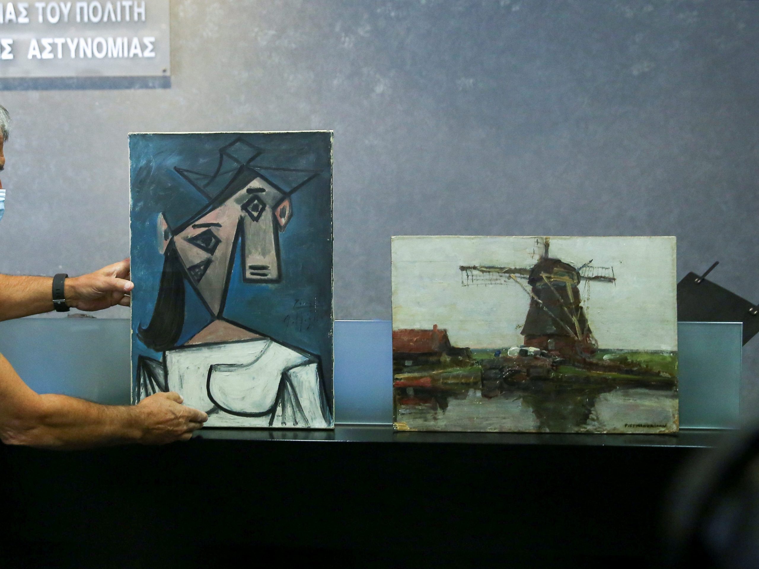 A man displays "Woman's Head" by Pablo Picasso and "Mill" by Piet Mondrian" in a museum.