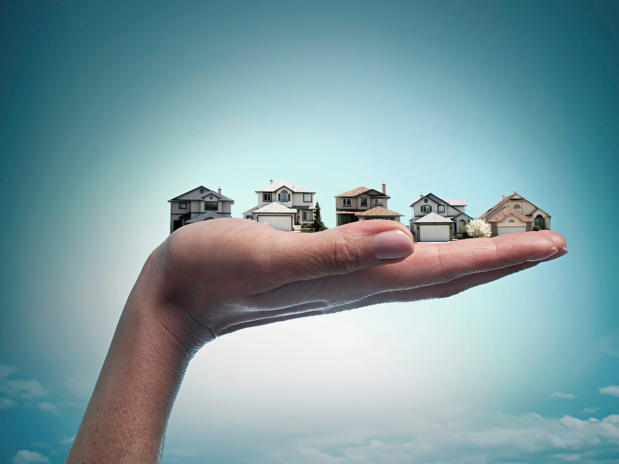 A hand holds up a row of houses in this photo illustration.