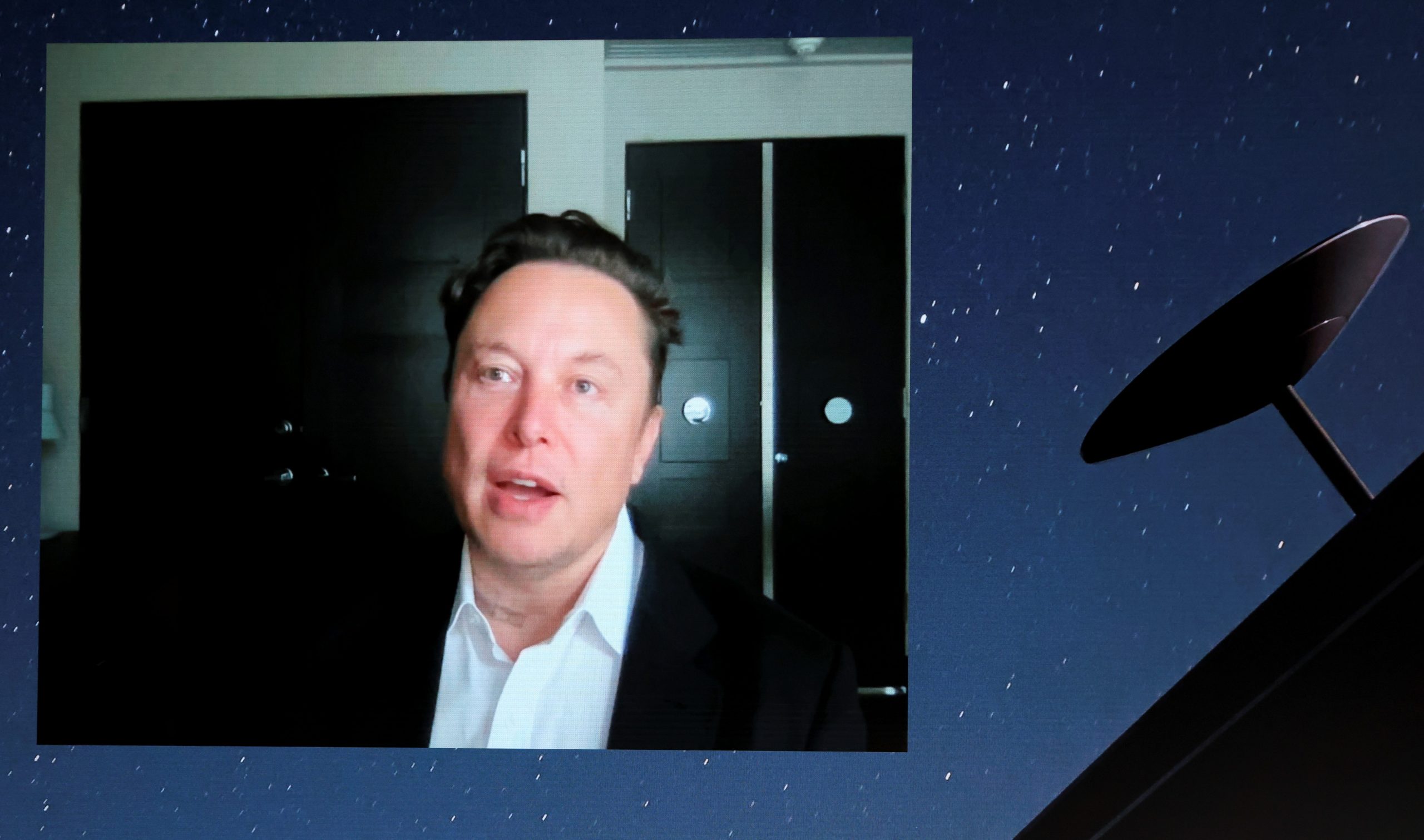 SpaceX founder Elon Musk speaking on a video call is projected onto a large screen.
