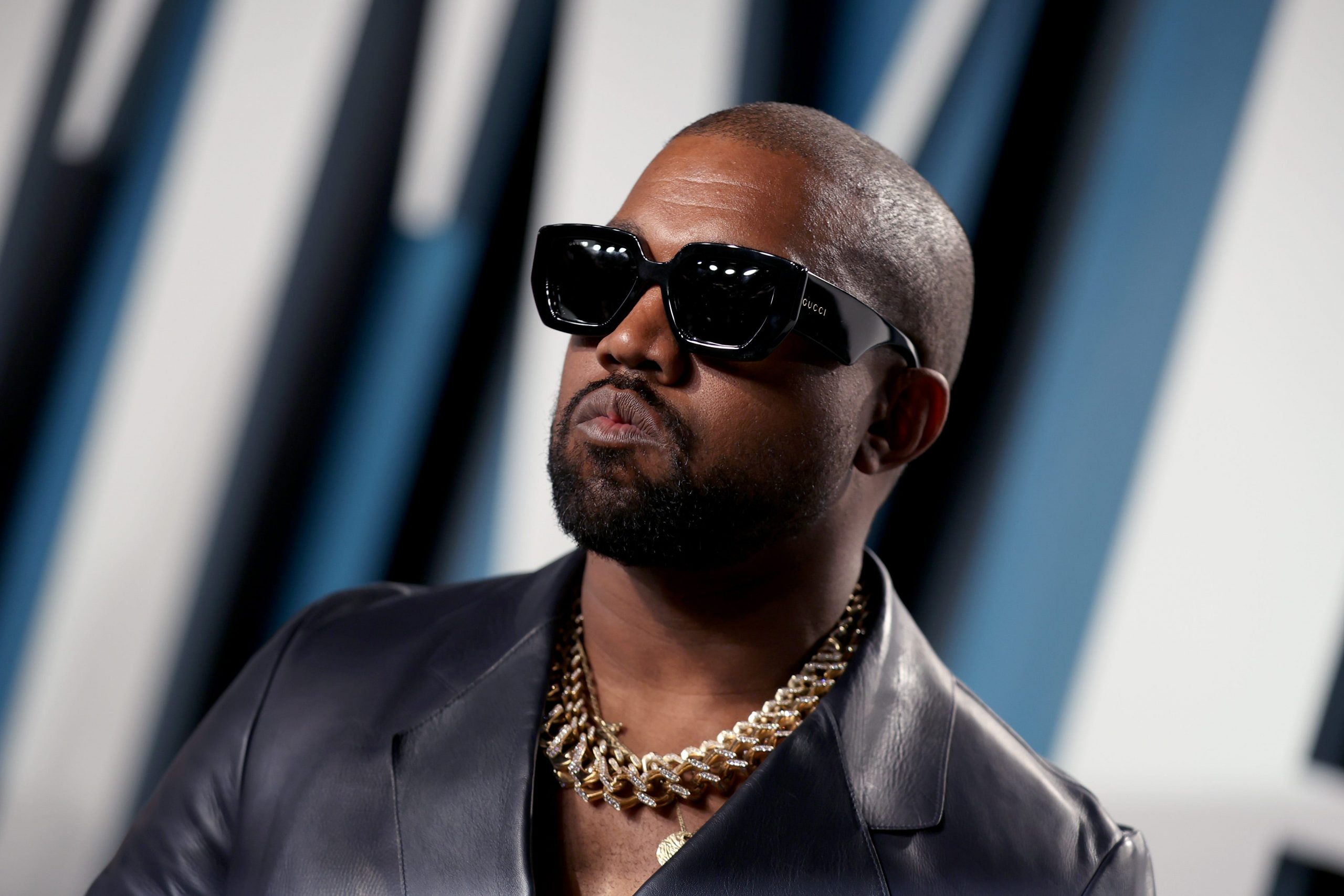 Kanye West wears sunglasses and a gold necklace at an event.