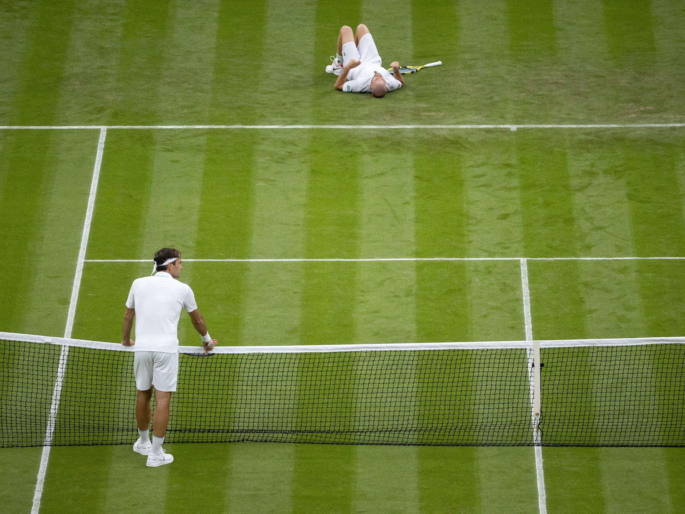 Roger Federer watches his fallen opponent Adrian Mannarino during the first round of Wimbledon.