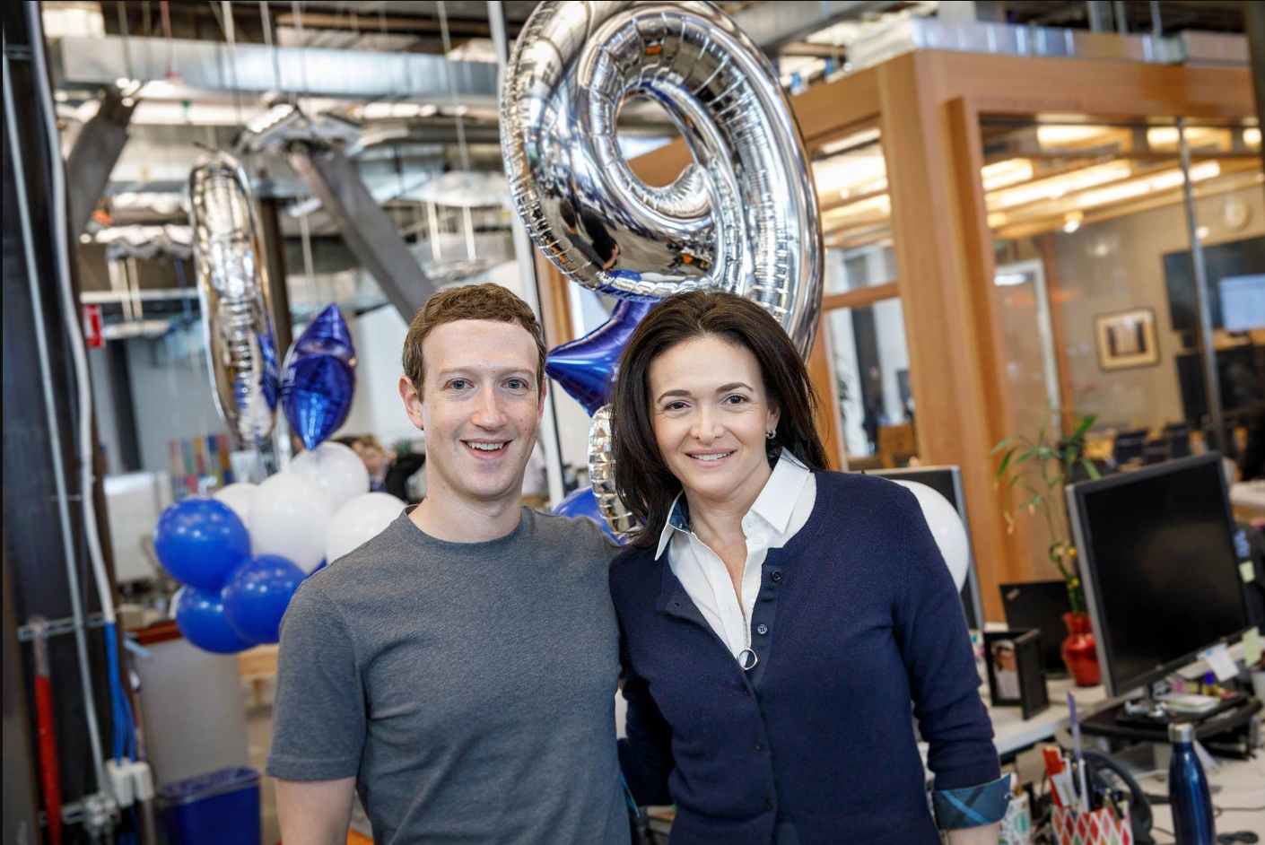 Mark Zuckerberg and Sheryl Sandberg stand in front of silver and blue balloons.
