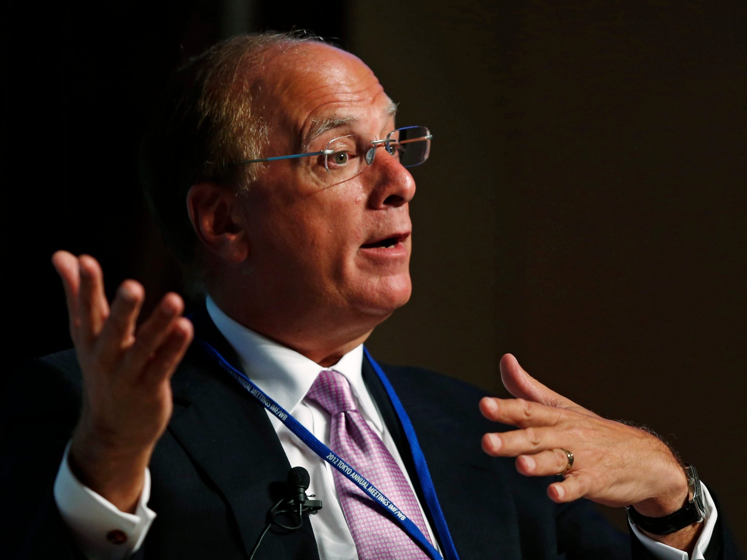 Larry Fink gesturing to his right in front of a black background.