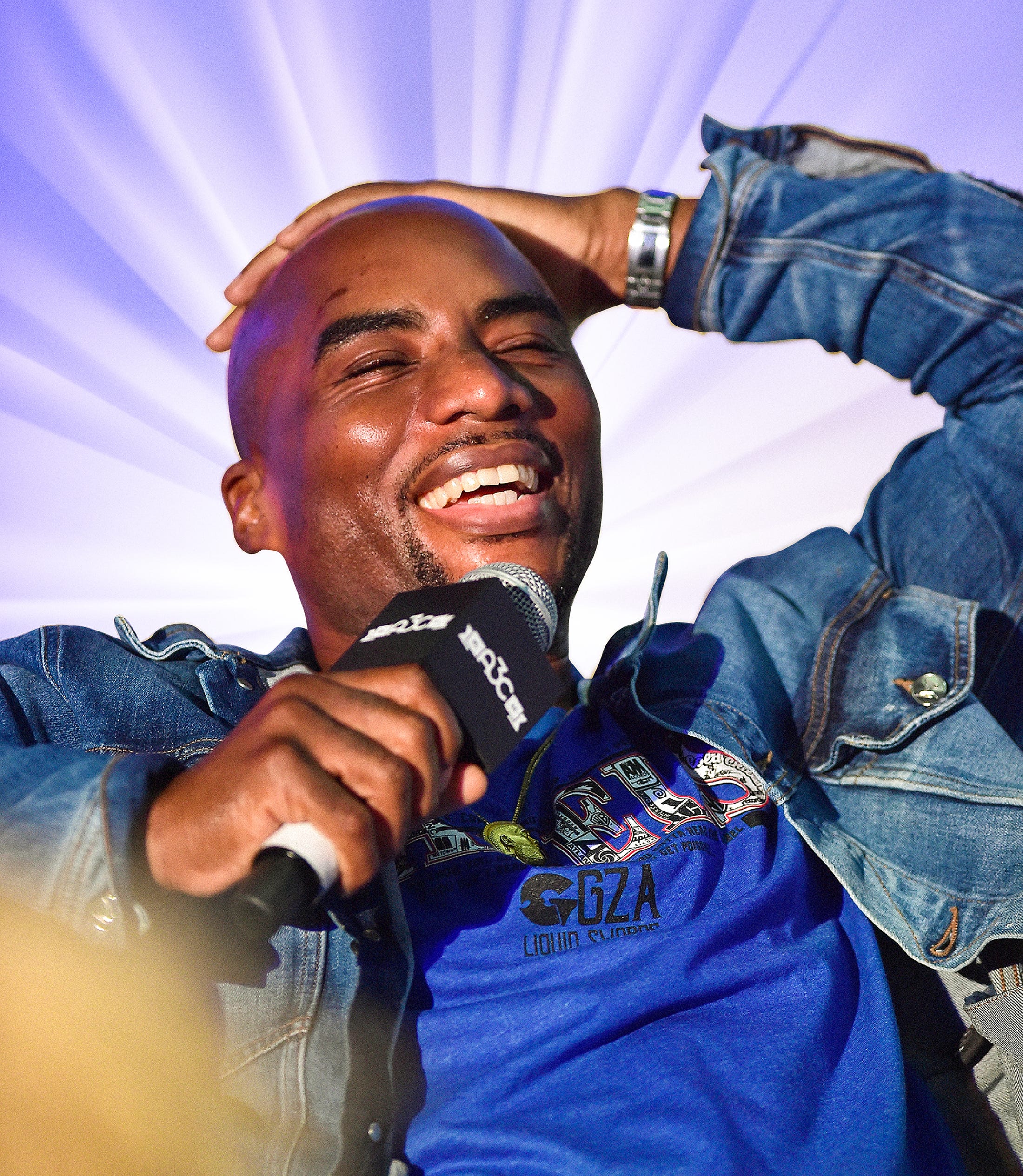 Charlamagne Tha God laughing during an interview with a golden light radiating from behind him.