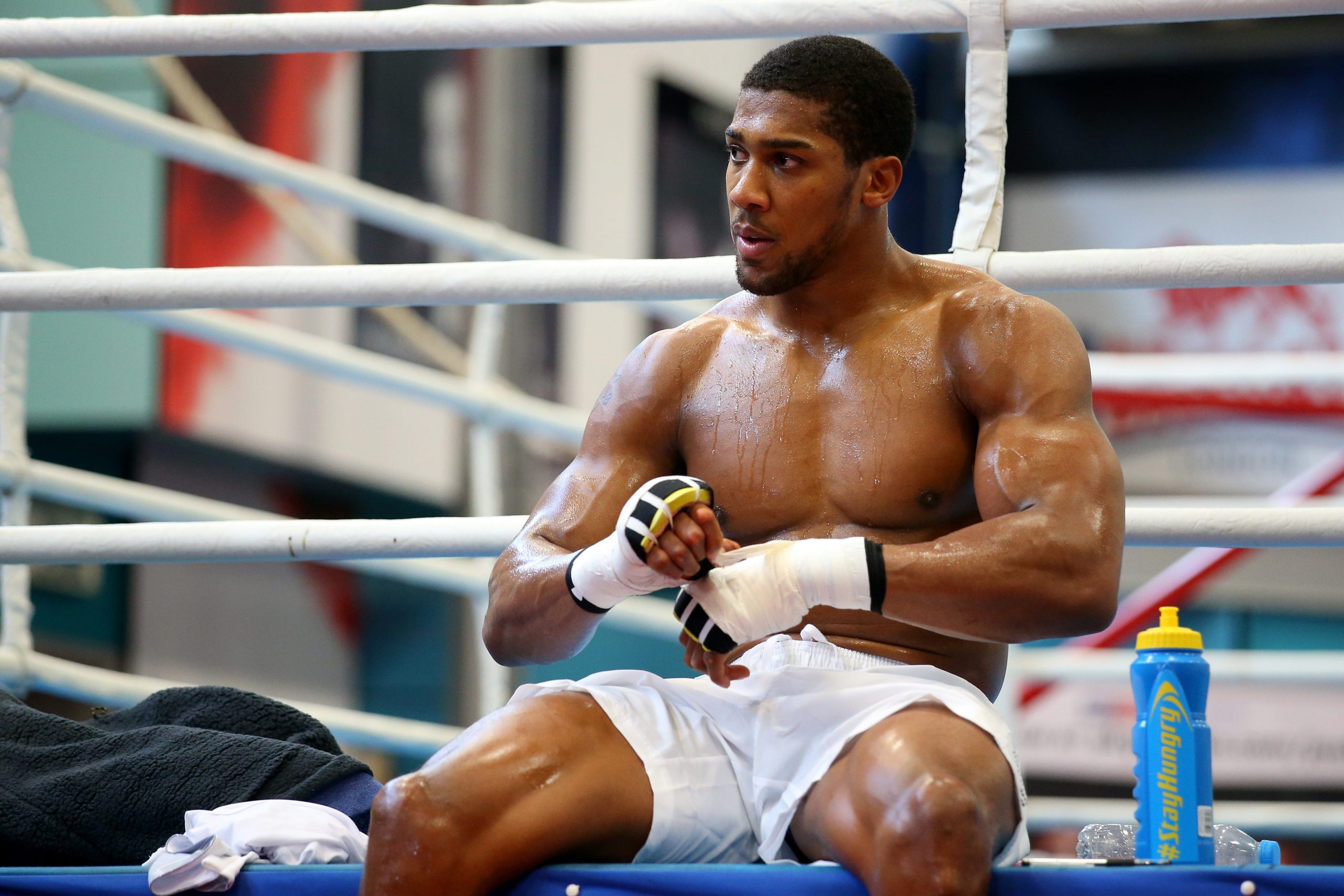 Anthony Joshua sitting on the edge of a boxing ring wrapping up his hands.