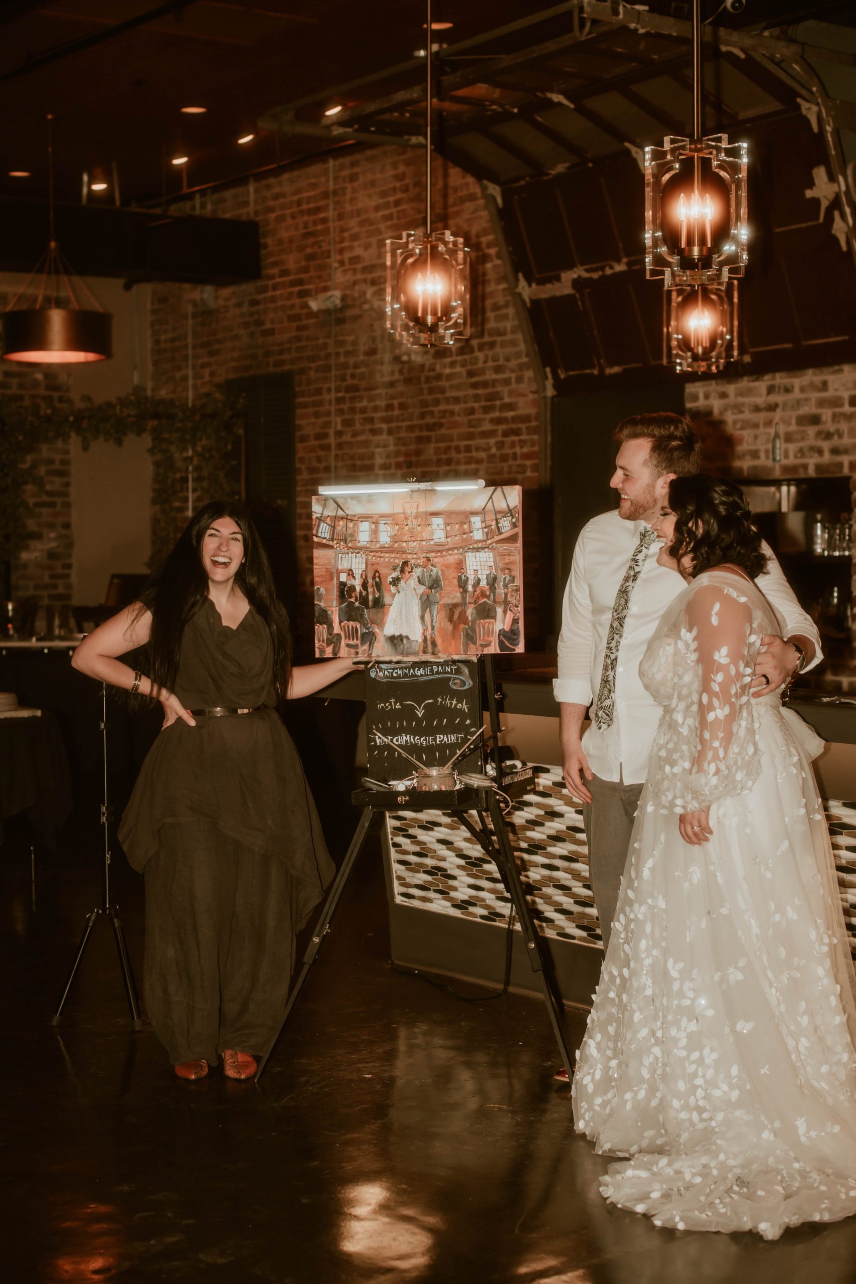 Live wedding painter Maggie stands next to her finished artwork of bride Reagan Sumrall and her husband Joseph Thompson.