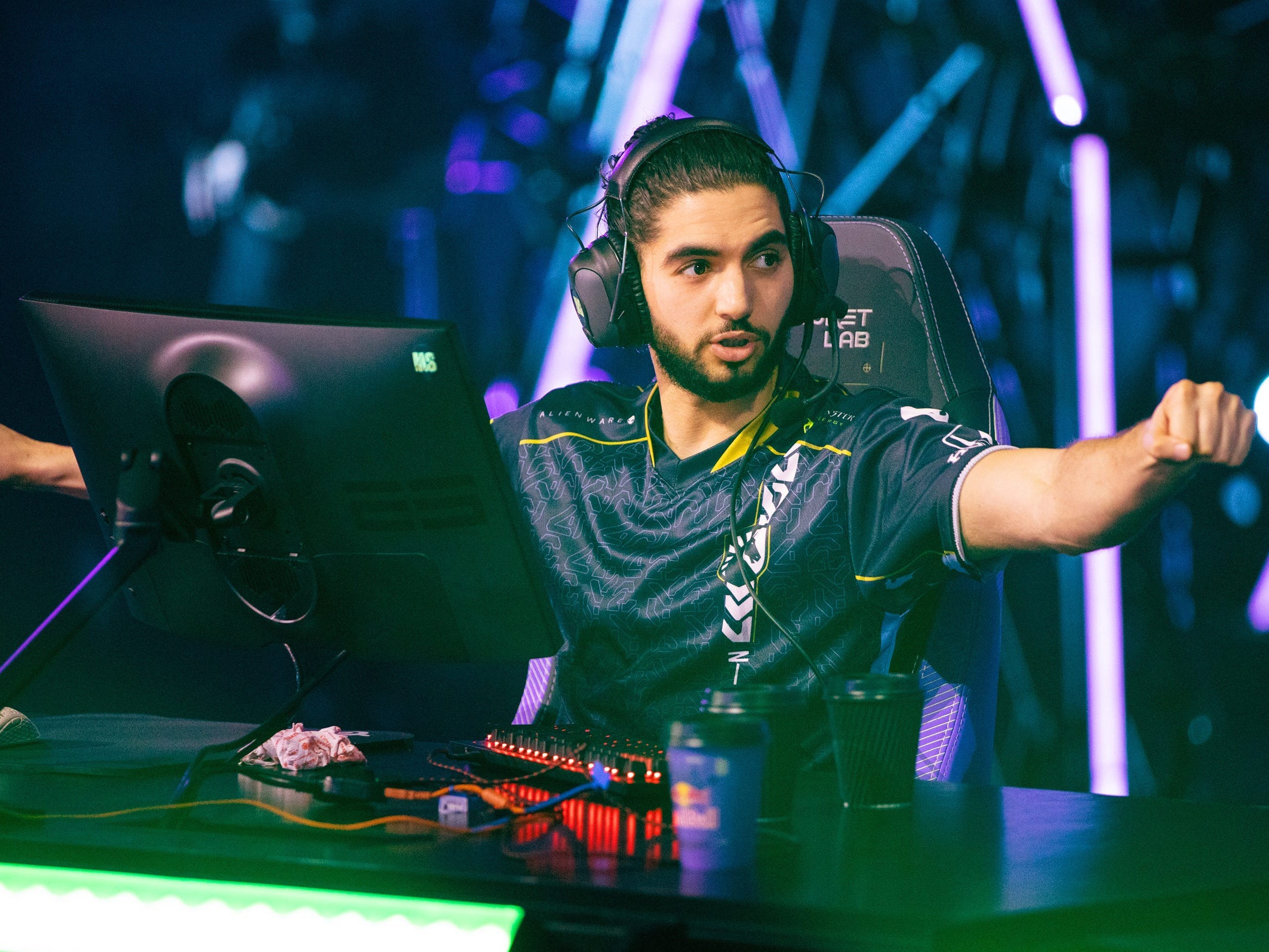 Adil "ScreaM" Benrlitom sits at a desk in front of a monitor. His arms are outstretched to first bump his teammates