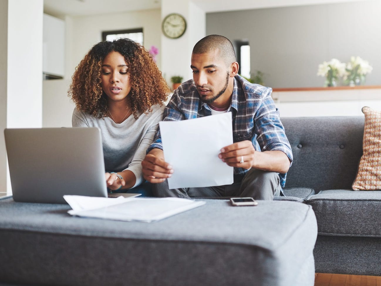 A couple looks at paperwork and a laptop while sitting on the couch.