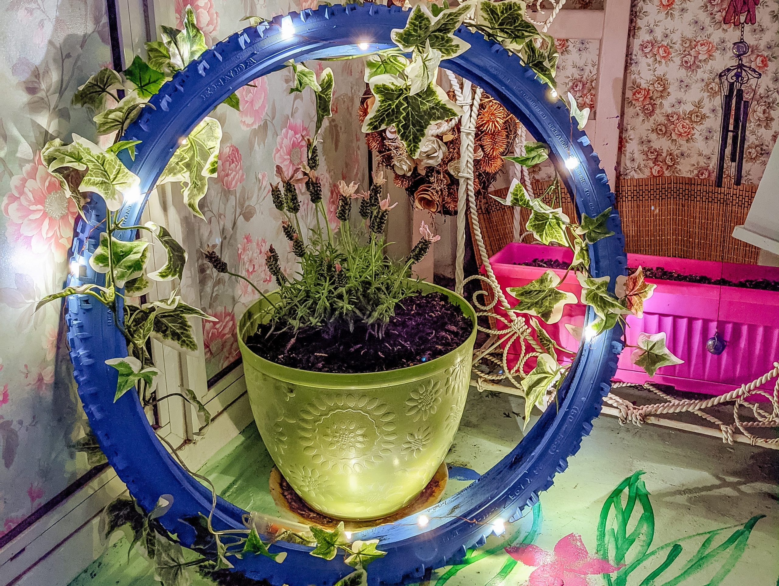 A blue tire covered in string lights and faux plants.