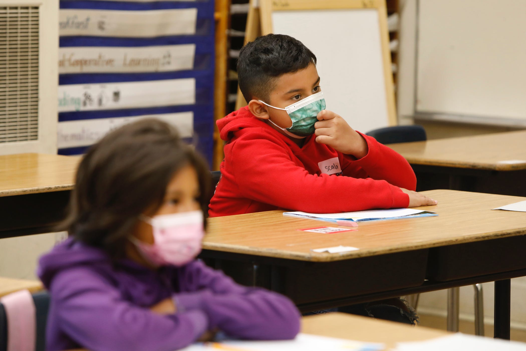 two students sitting at their desks, wearing masks