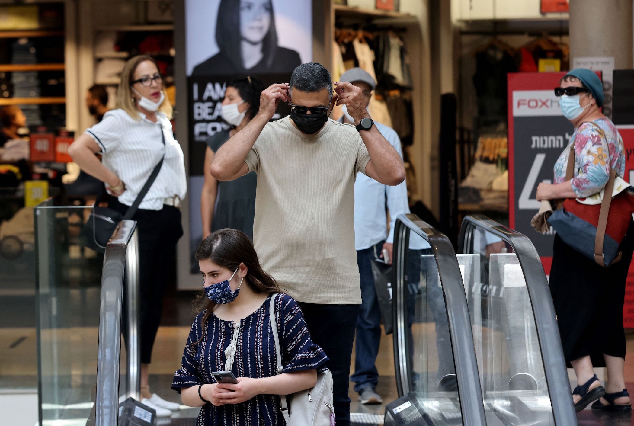 people wear face masks as they ride an escalator in a shopping mall