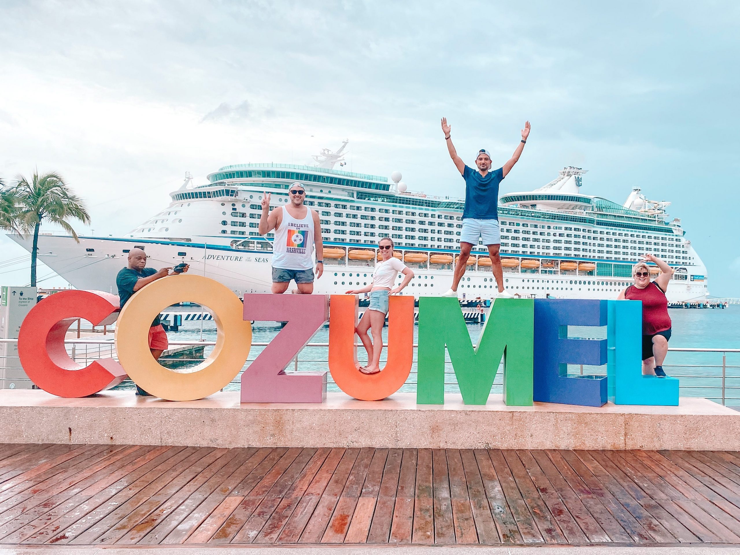 3 people standing on a giant Cozumel sign with a cruise ship in the background