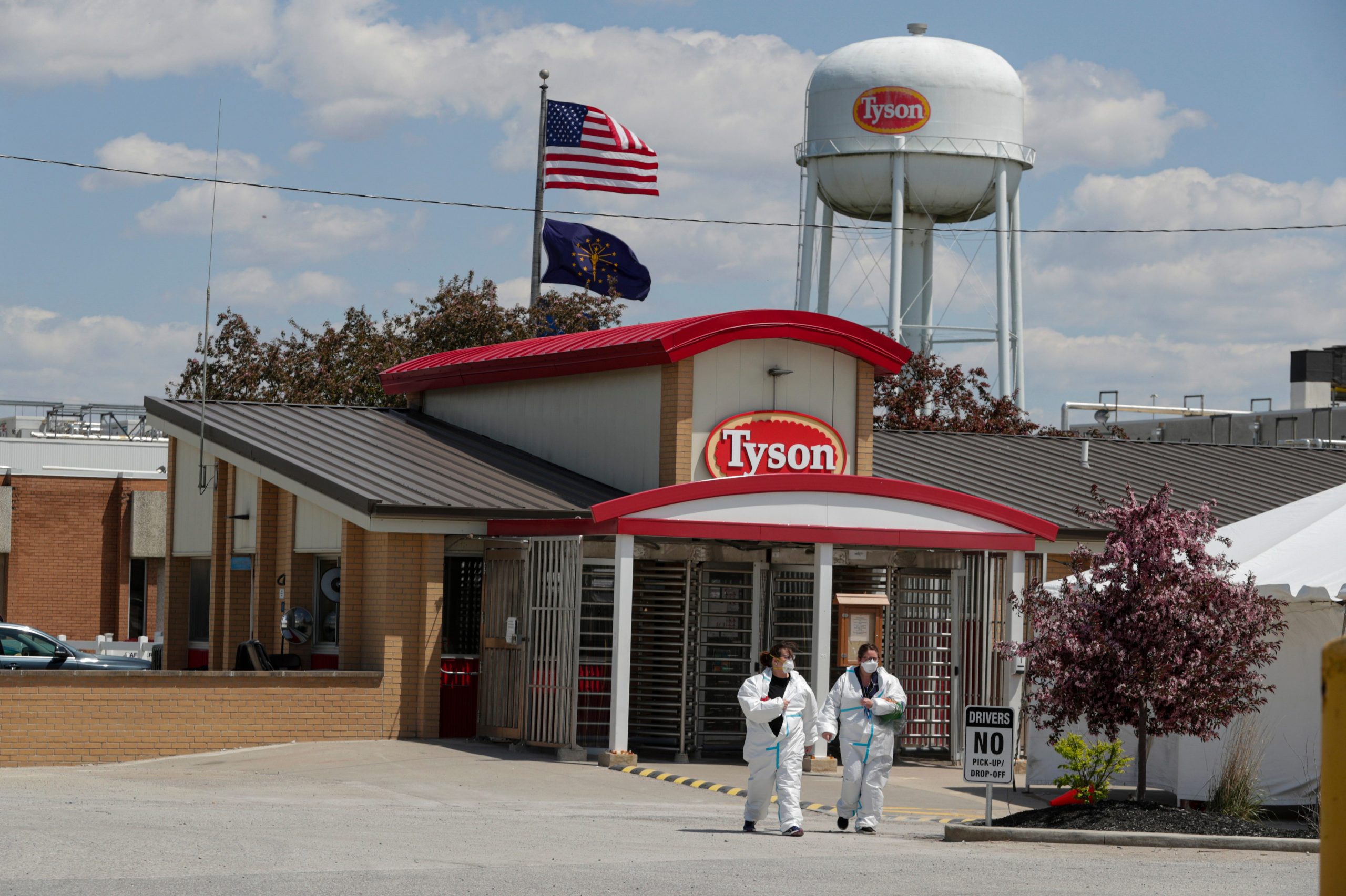 Two people wearing white jumpsuits leave a Tyson Foods facility on a sunny day in Indiana
