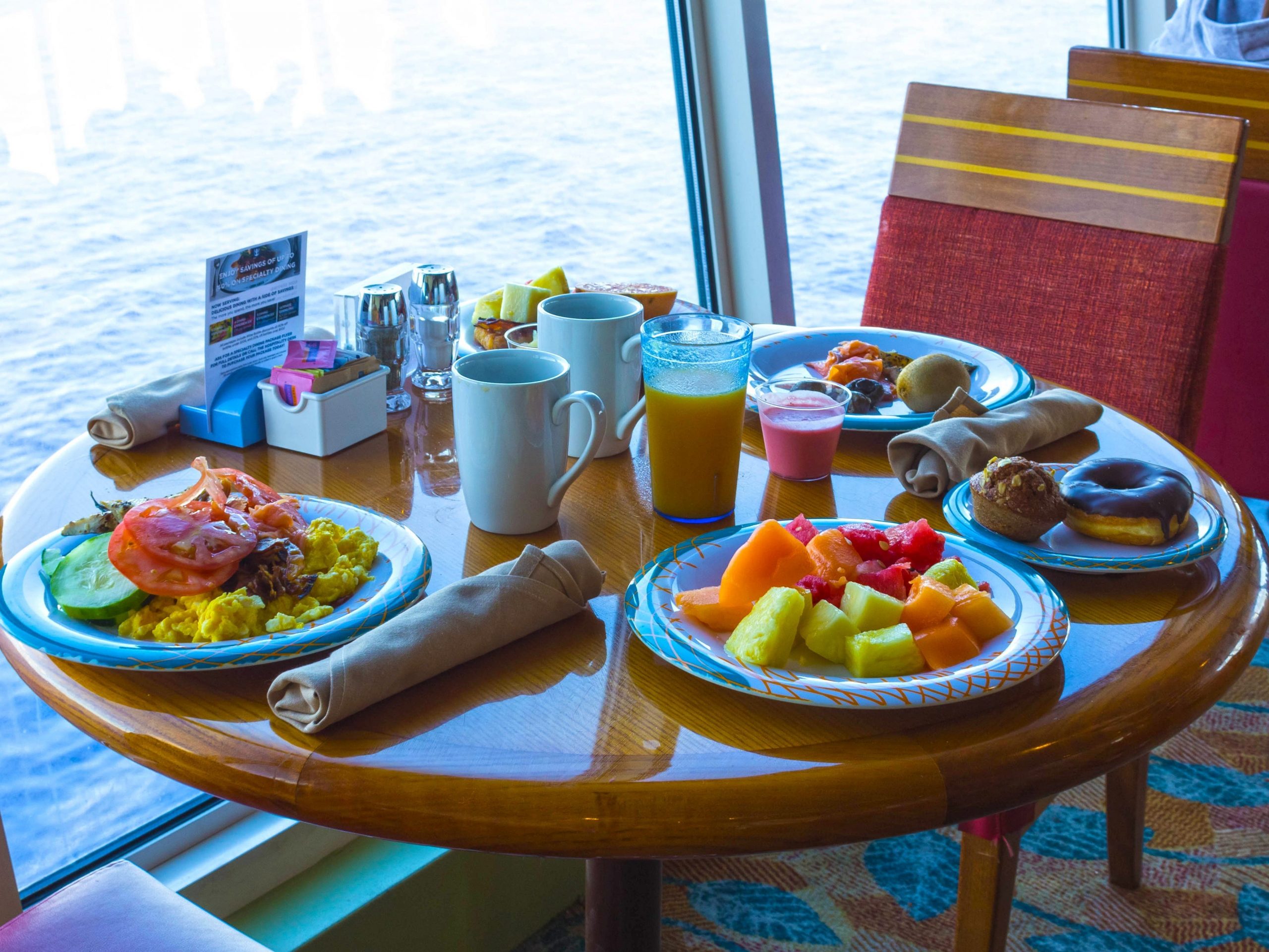 a wooden, circular table full of food with the ocean in the background