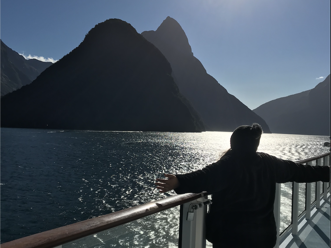 a person standing at the railing of a ship looking at the ocean and mountains