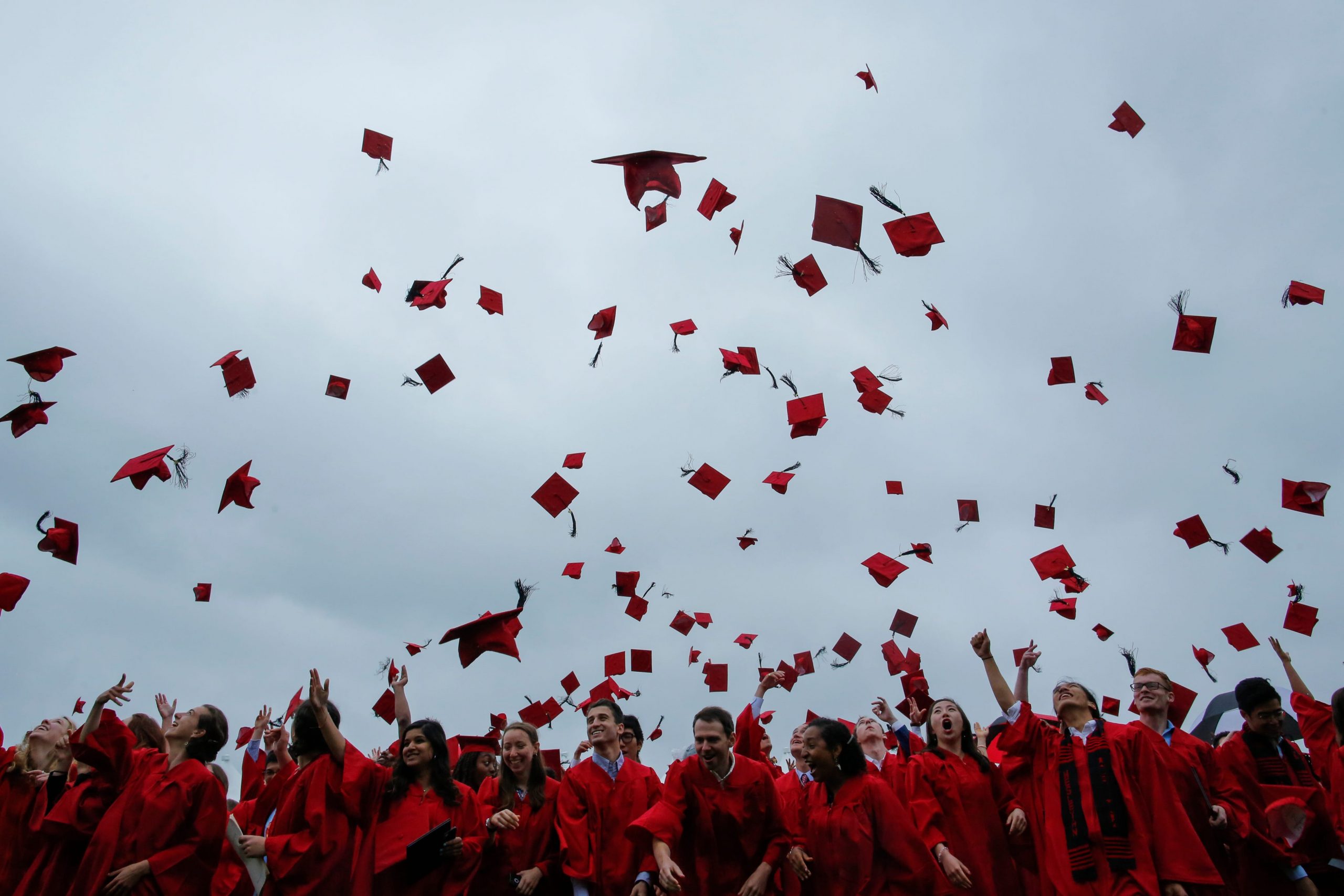 Hundreds of graduation hats are seen in the air above a crowd of students in graduation garb.