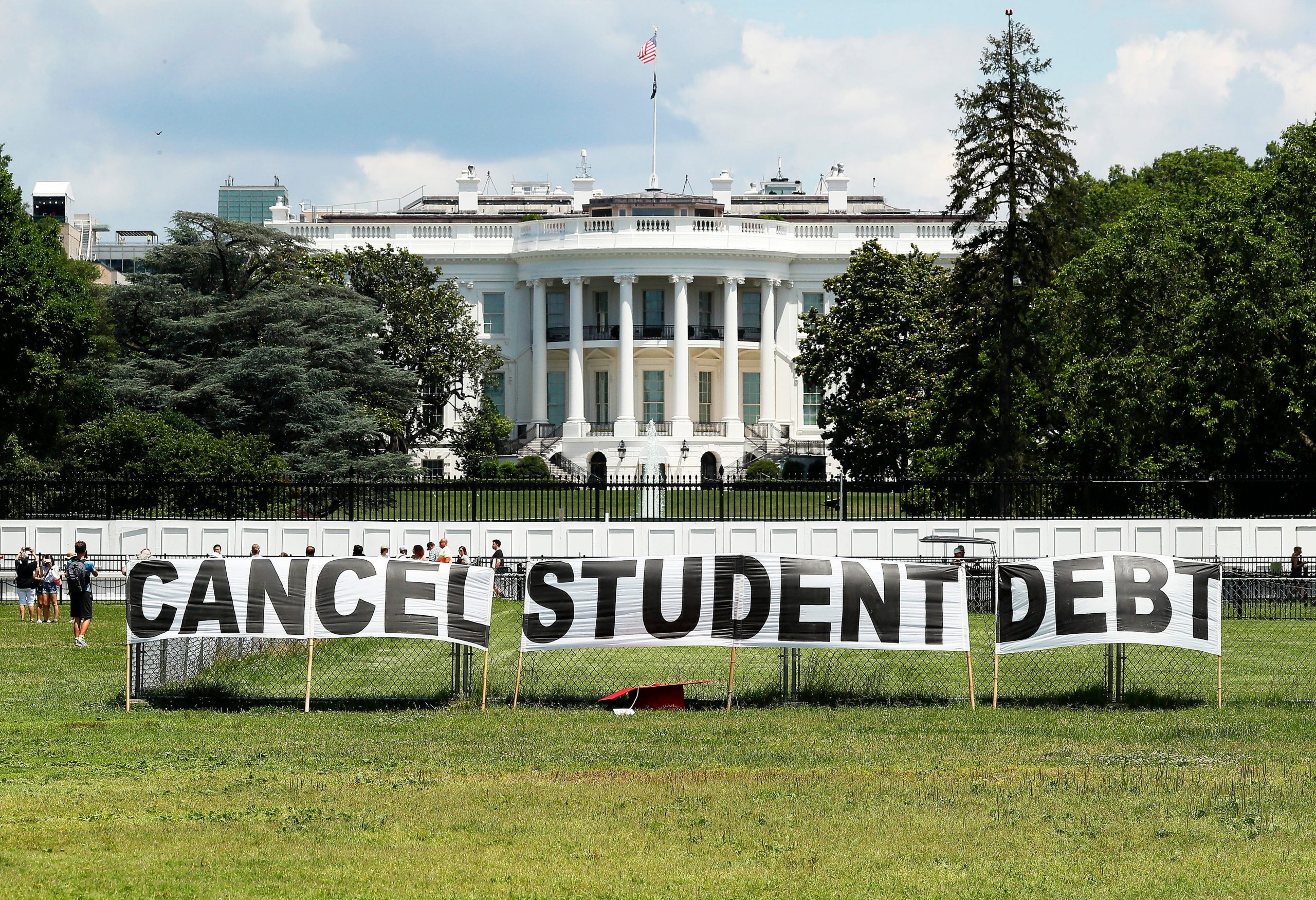 A hand-written sign reading "Cancel Student Debt" is held up and the White House is seen in the background.