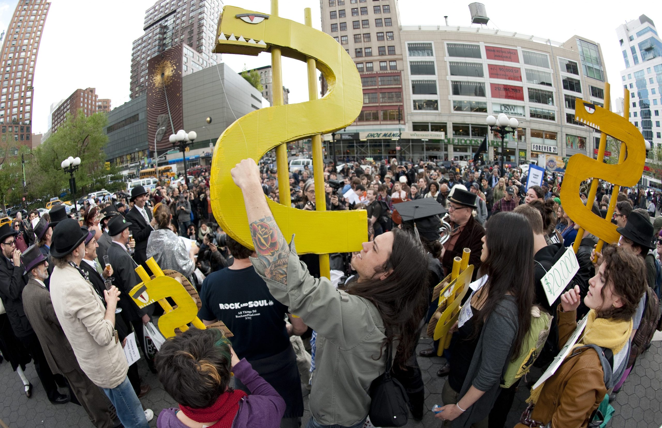 A crowd of people are seen, some holding hand-made paper dollar signs.