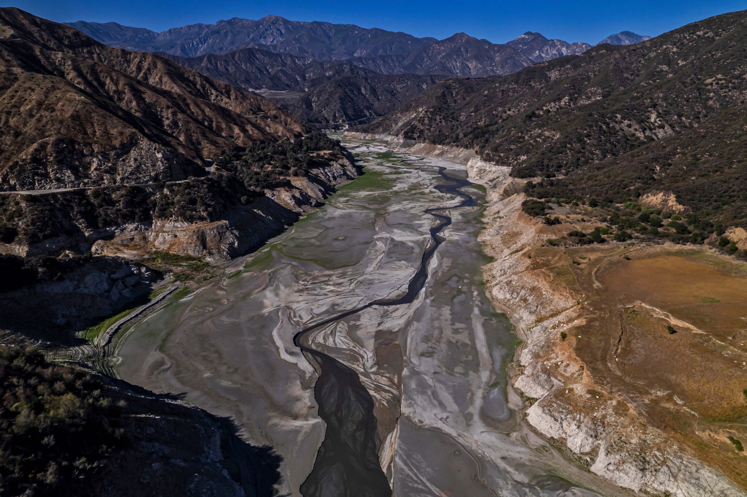 An aerial view of reservoir tucked in between a mountainous landscape under a bright sky.