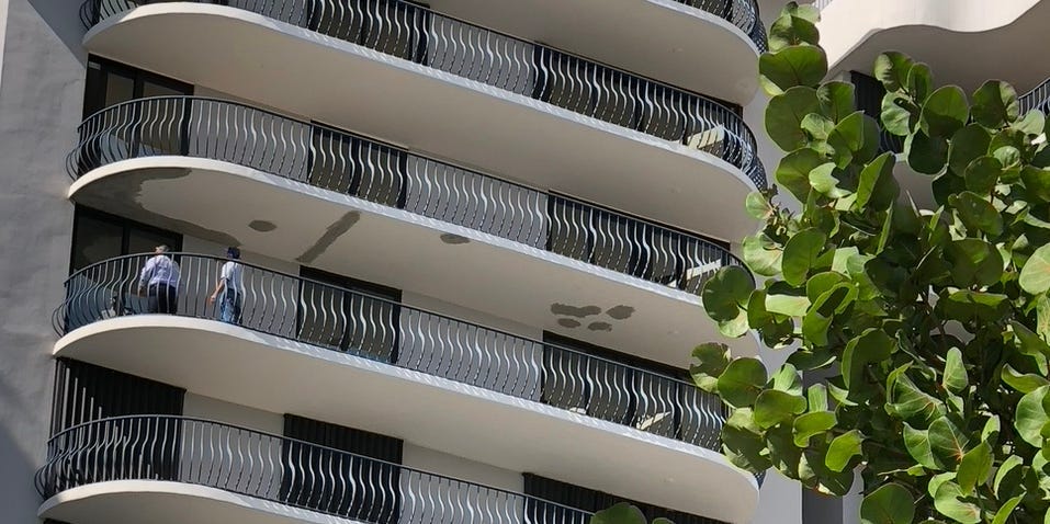 Two men inspect the bottom of a balcony.