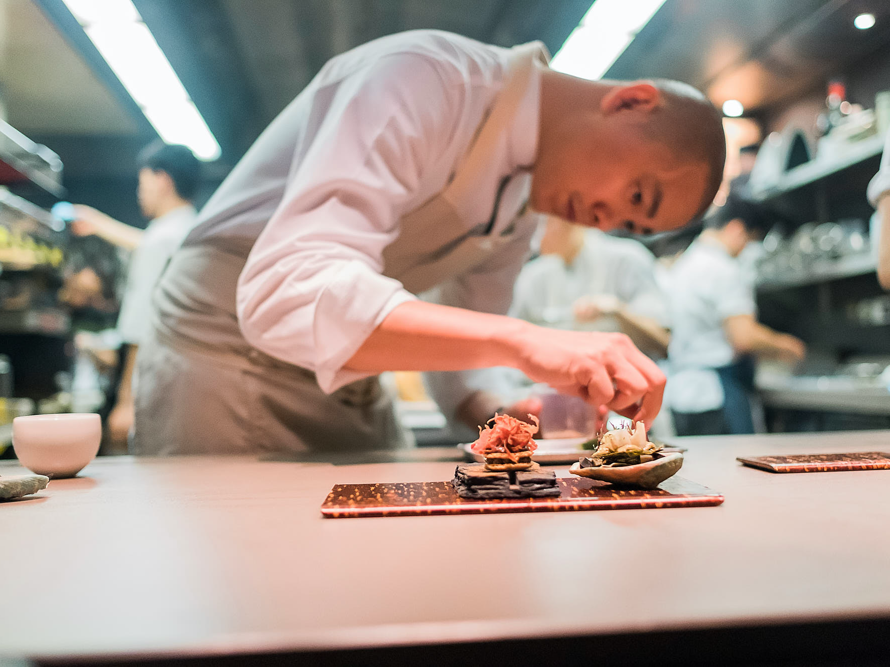 Chef Andre Chiang bending over a dish in his kitchen in Singapore to garnish a dish.