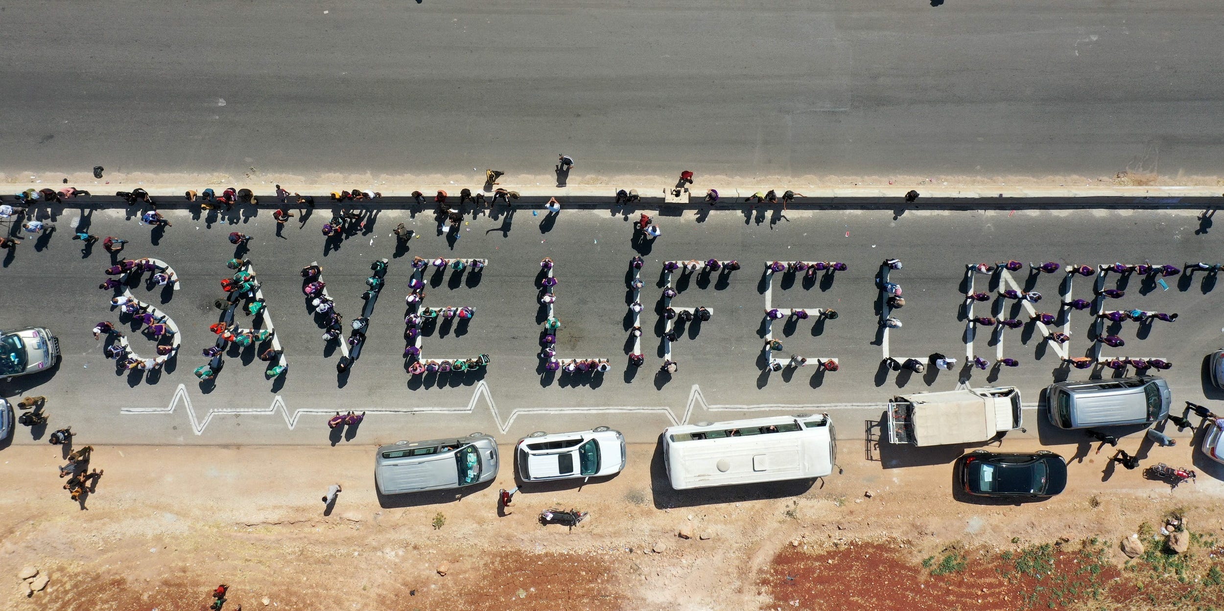 A human chain is formed by workers from the civil society, humanitarian aid, and medical and rescue services in a vigil calling for maintaining a UN resolution authorising the passage of humanitarian aid into Syria's rebel-held northwestern province of Idlib through the Bab al-Hawa border crossing with Turkey, near Bab al-Hawa along the motorway linking it to the city of Idlib on July 2, 2021. - The UN resolution is set to expire on July 10 -- by which time the Security Council must have voted on its renewal, which is currently threatened by a veto from Russia on grounds that it violates Syria's sovereignty, in a bid to re-route aid through regime-controlled territory.