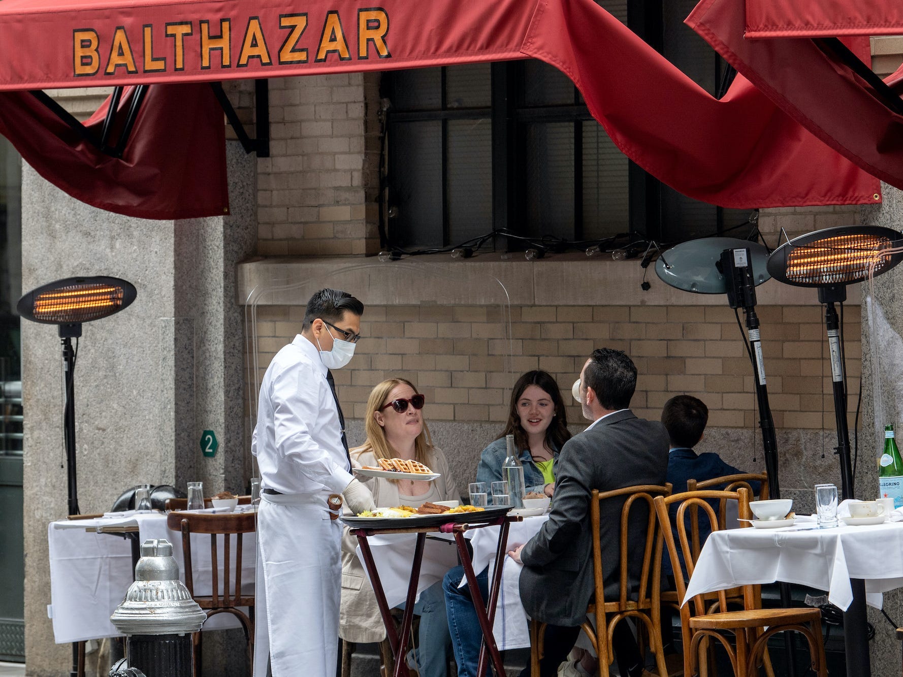 A waiter wearing a mask is serving customers who are sitting down at a table.