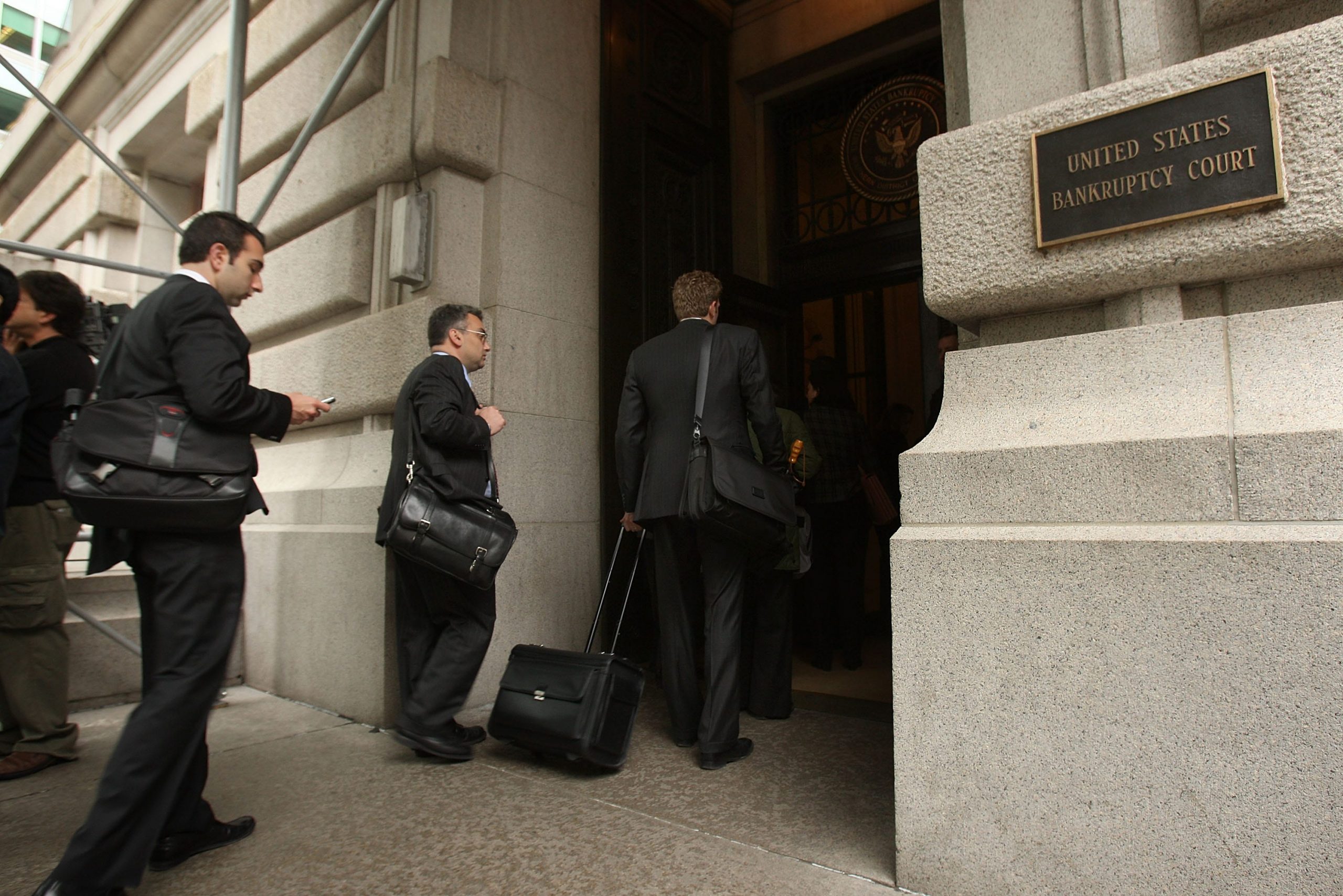 Men in suits and large bags enter a building, marked United States Bankruptcy Court