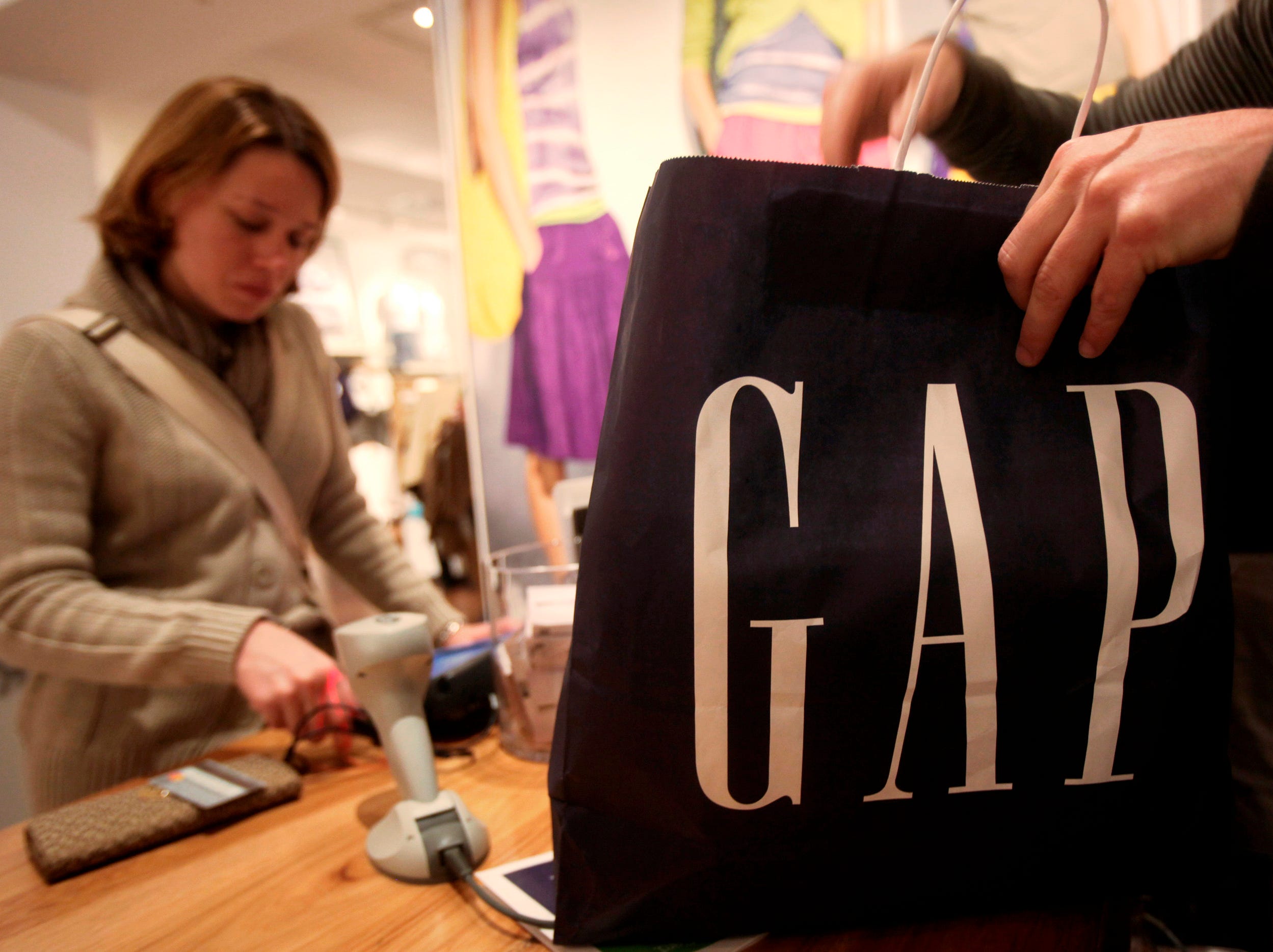 A Gap employee packs shopping in a bag while a customer pays