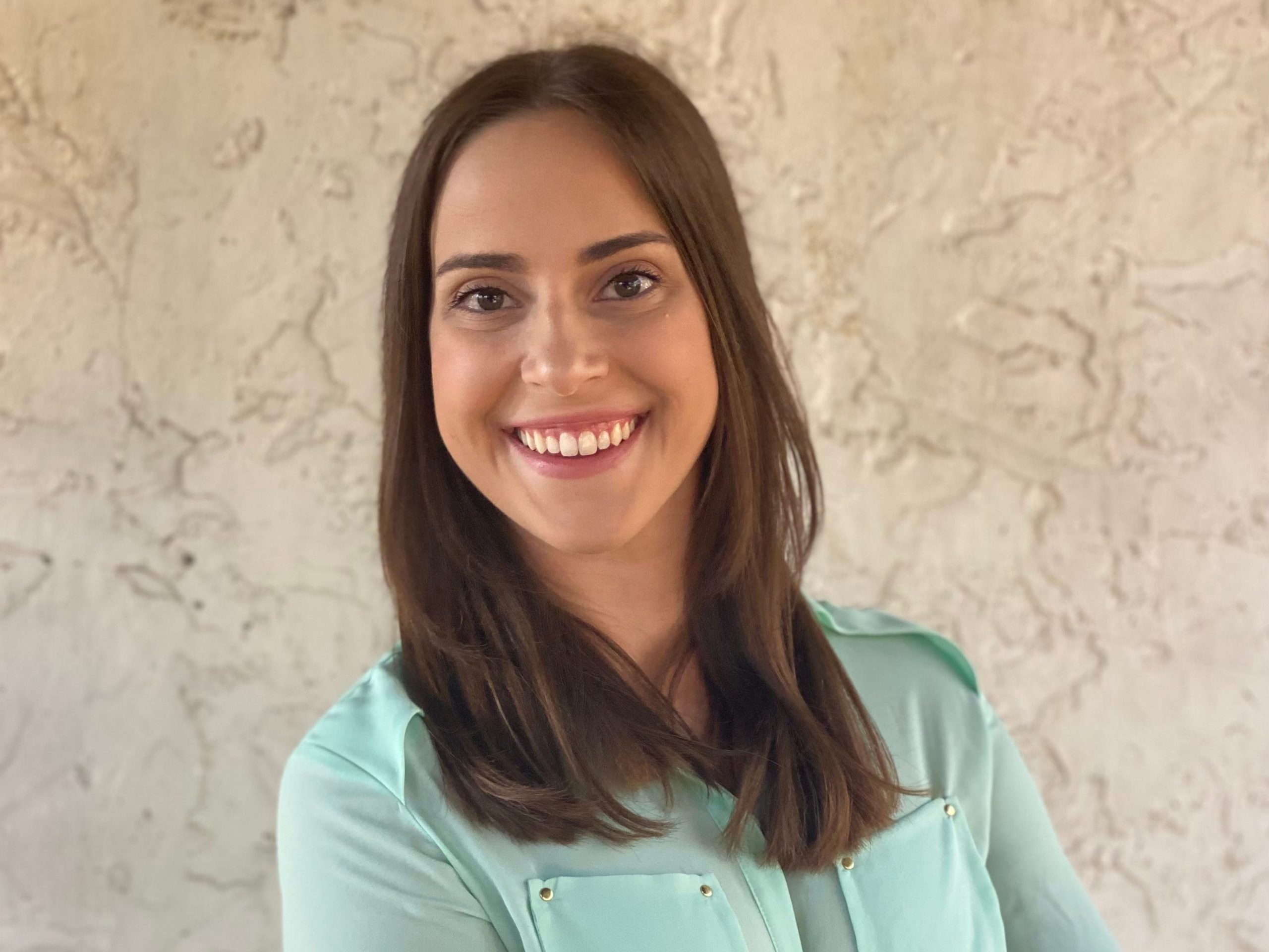 Melanie Anderson wears a green blouse while smiling at the camera