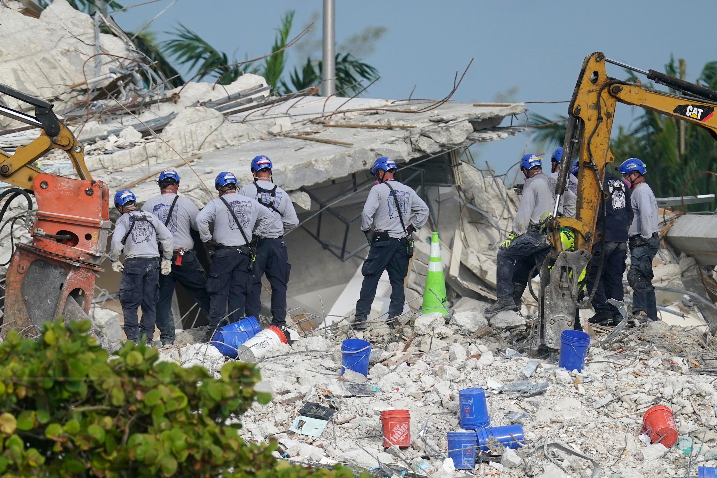 rescuers in hard hats look at rubble of the collapsed condo site