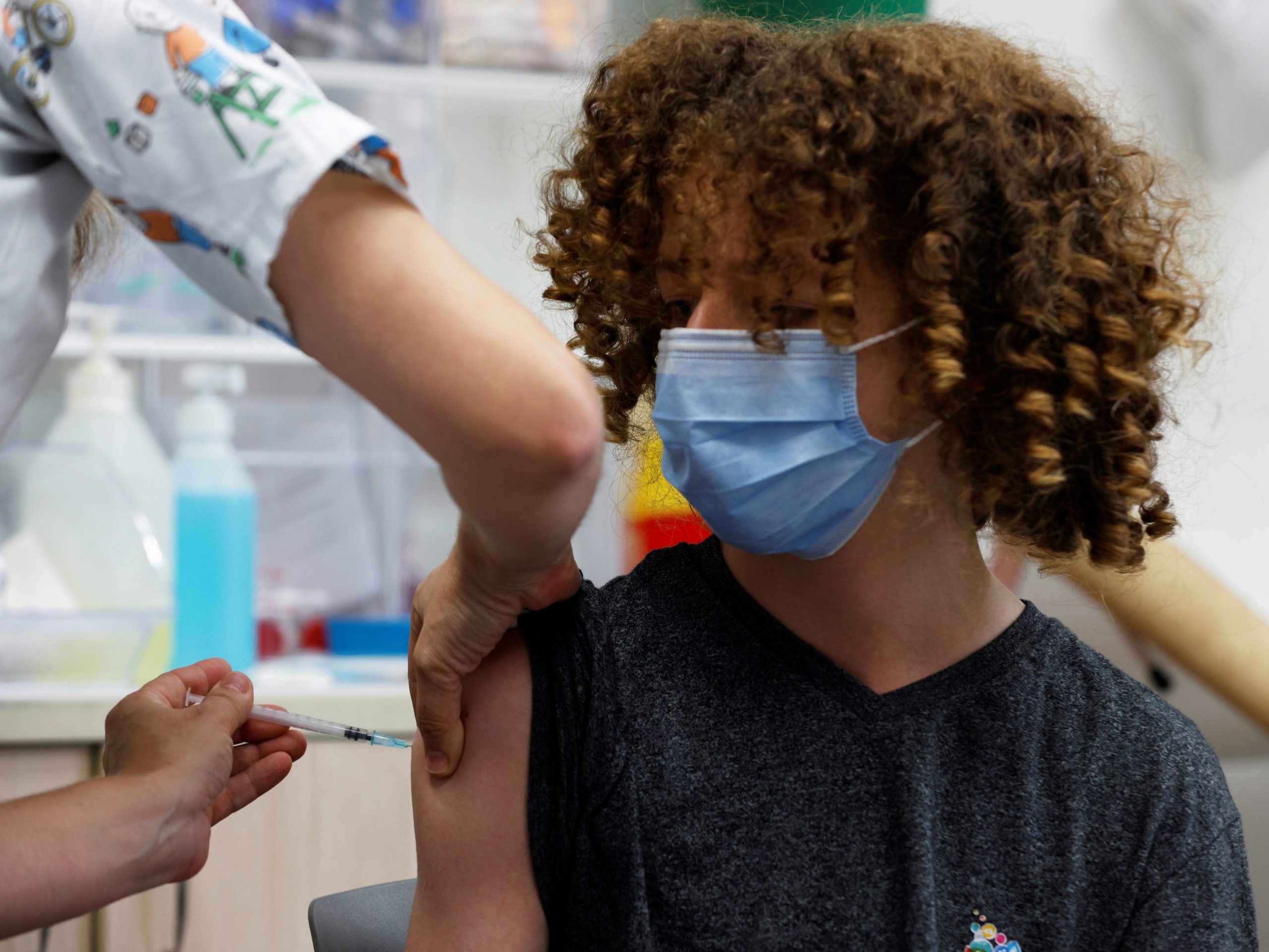 masked teenager with curly hair gets covid vaccine shot
