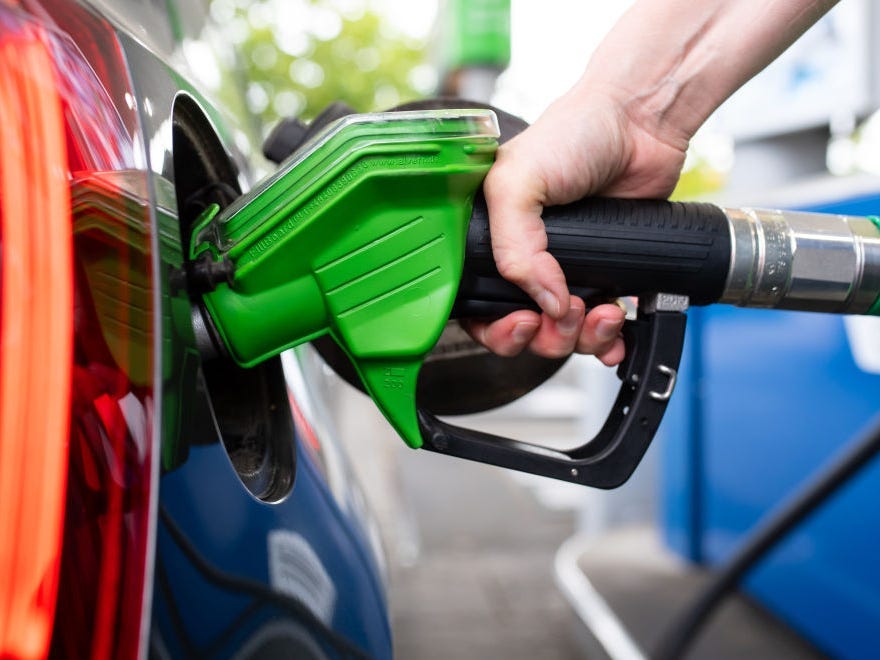 A woman holds a pump nozzle in her hand at a gas station and refuels a car.