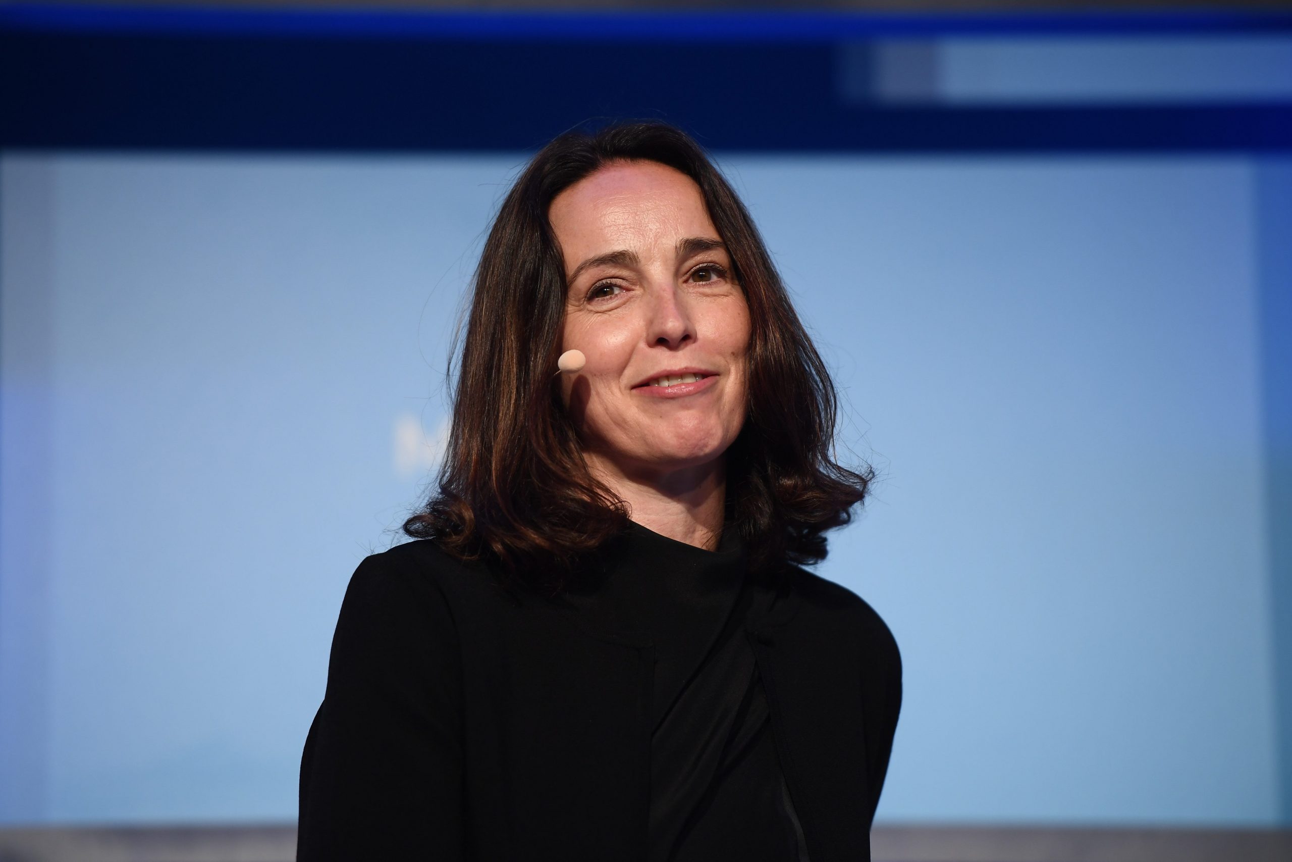 Nextdoor CEO Sarah Friar sits on stage in front of a blue background smiling.