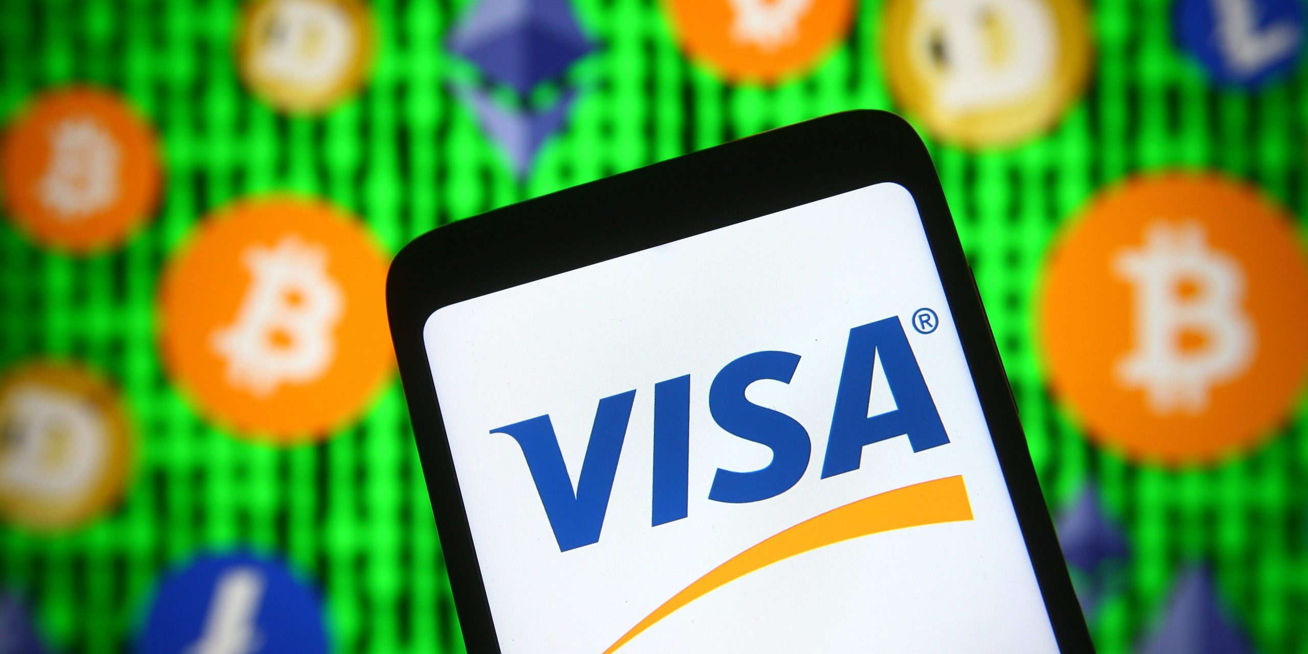 In this photo illustration, Visa logo is seen displayed on a smartphone screen in front of cryptocurrency signs.