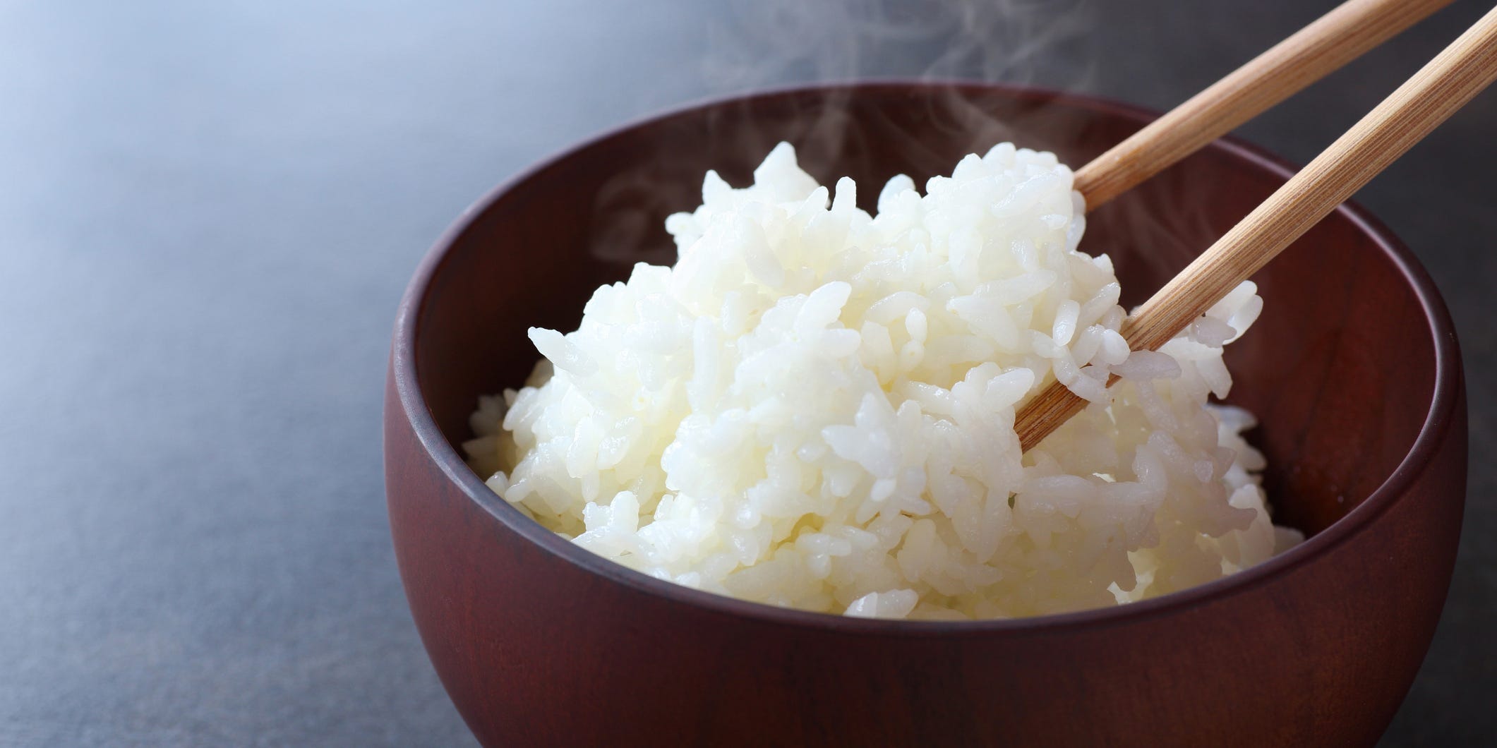 A pair of wooden chopsticks reaching into a steaming bowl of white rice