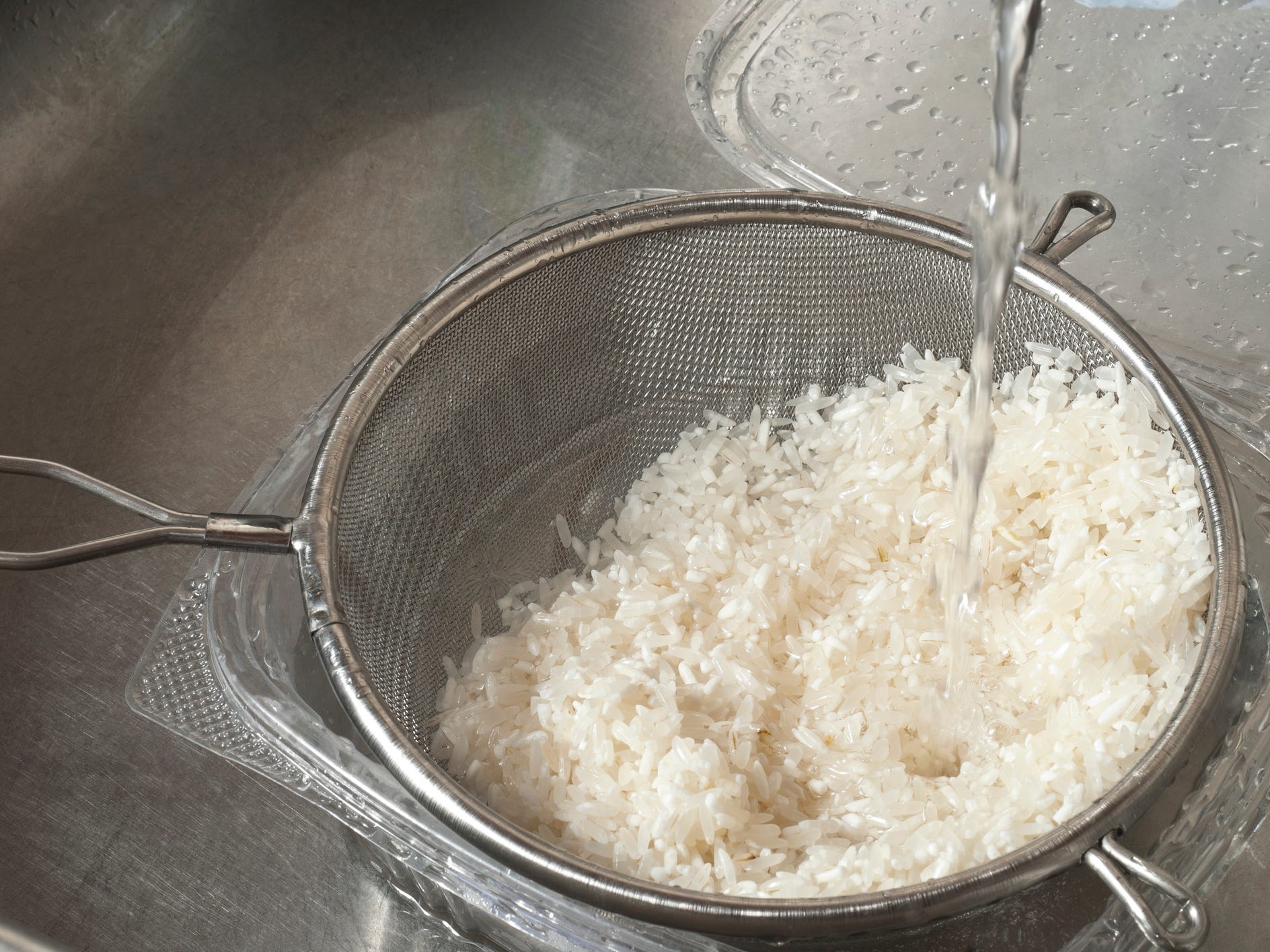 White rice in a strainer being rinsed in the sink